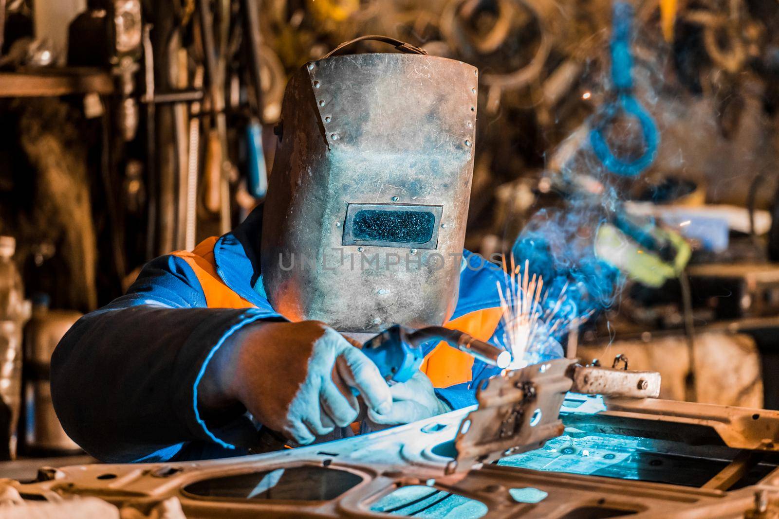 Welder in the shield worker is engaged in welding and metal work, repair of the car door at the industrial plant.