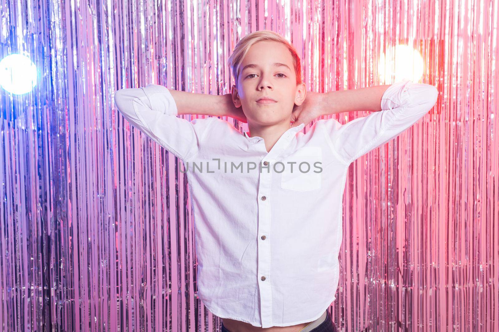 Awkward age and teenage concept - Portrait of teen boy at a party. Shiny background. by Satura86