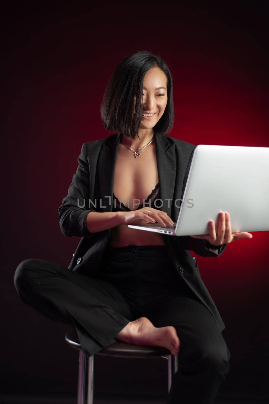 the asian woman in a jacket with a laptop in her hands on a bar stool in a dark red background