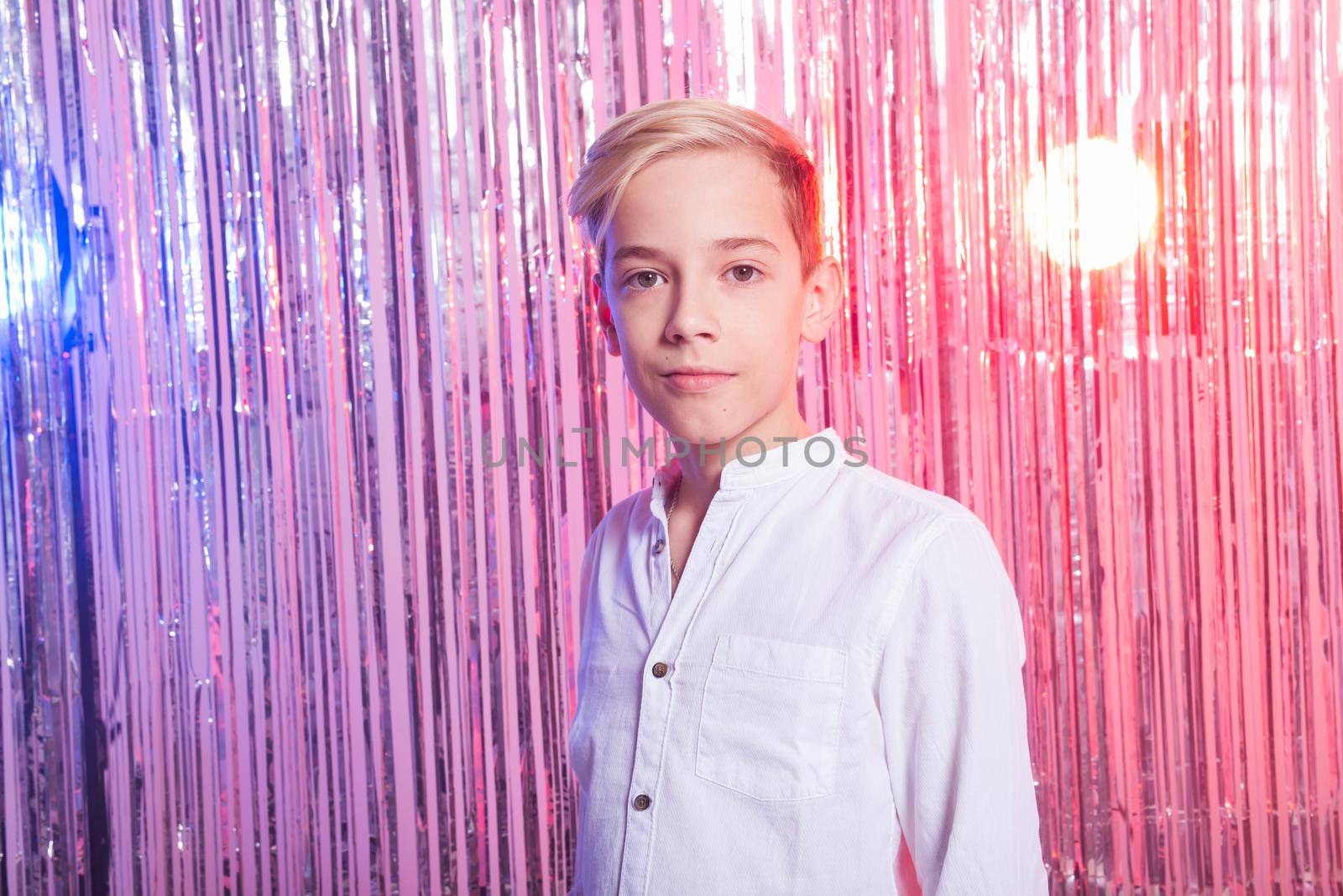 Awkward age and teenage concept - Portrait of teen boy at a party. Shiny background. by Satura86