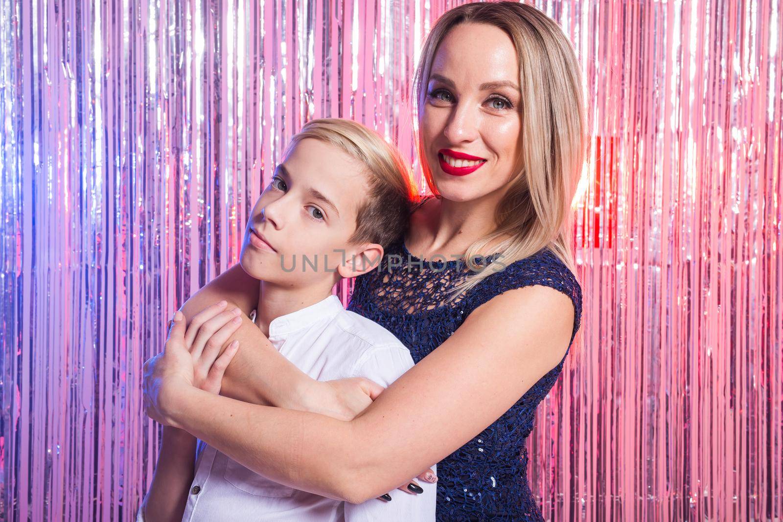 Mothers day, children and family concept - teen boy hugging his mom on shiny party background