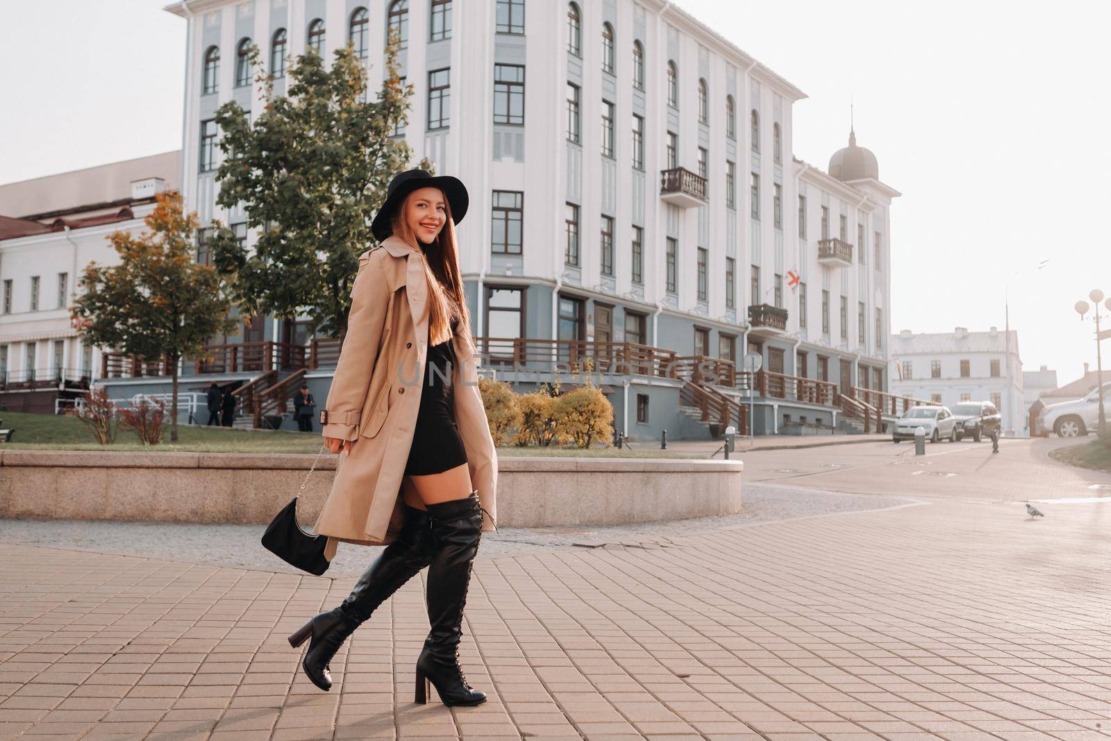 Stylish young woman in a beige coat in a black hat on a city street. Women's street fashion. Autumn clothing.Urban style by Lobachad