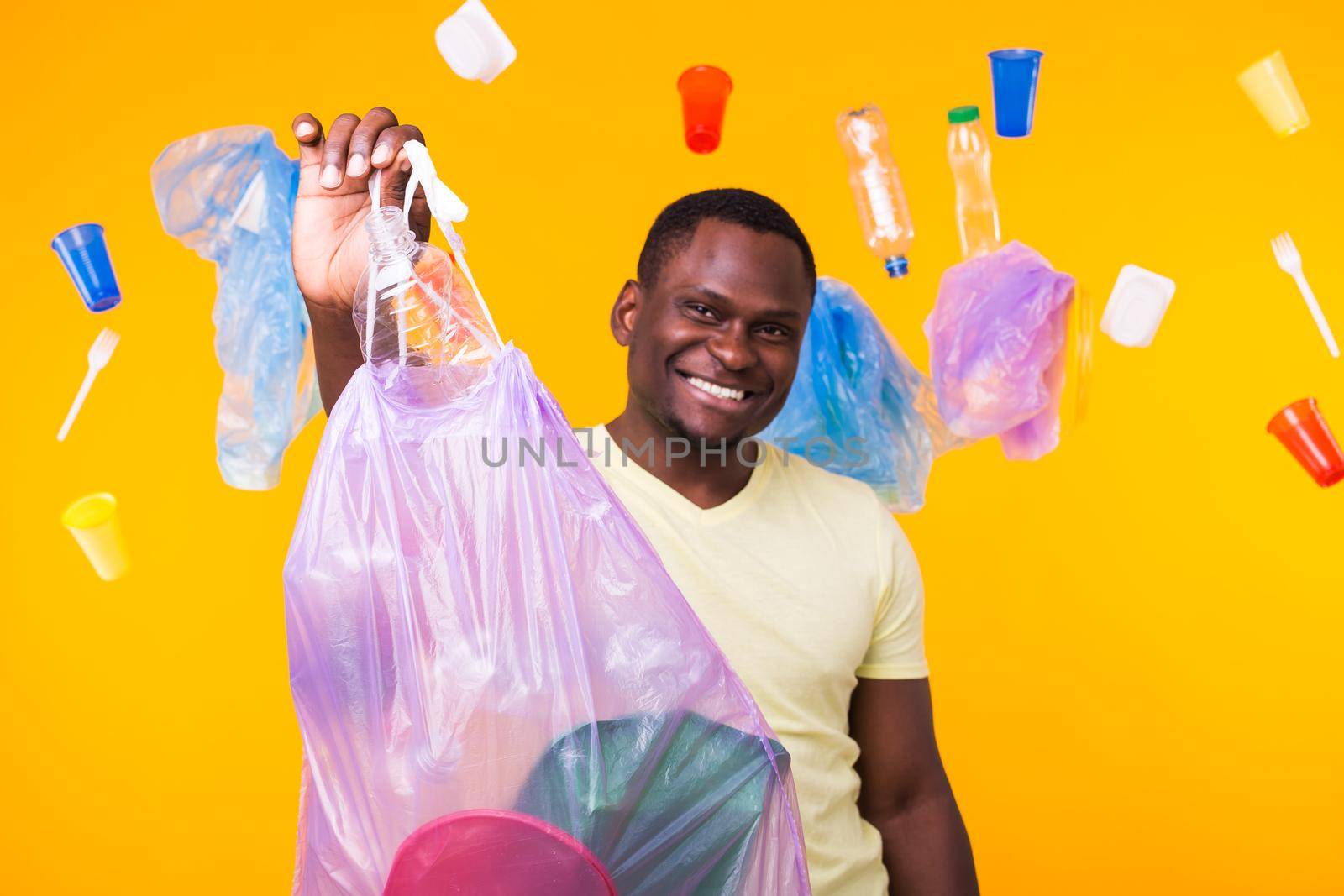 Problem of trash, plastic recycling, pollution and environmental concept - happy african american man carrying garbage for recycling on yellow