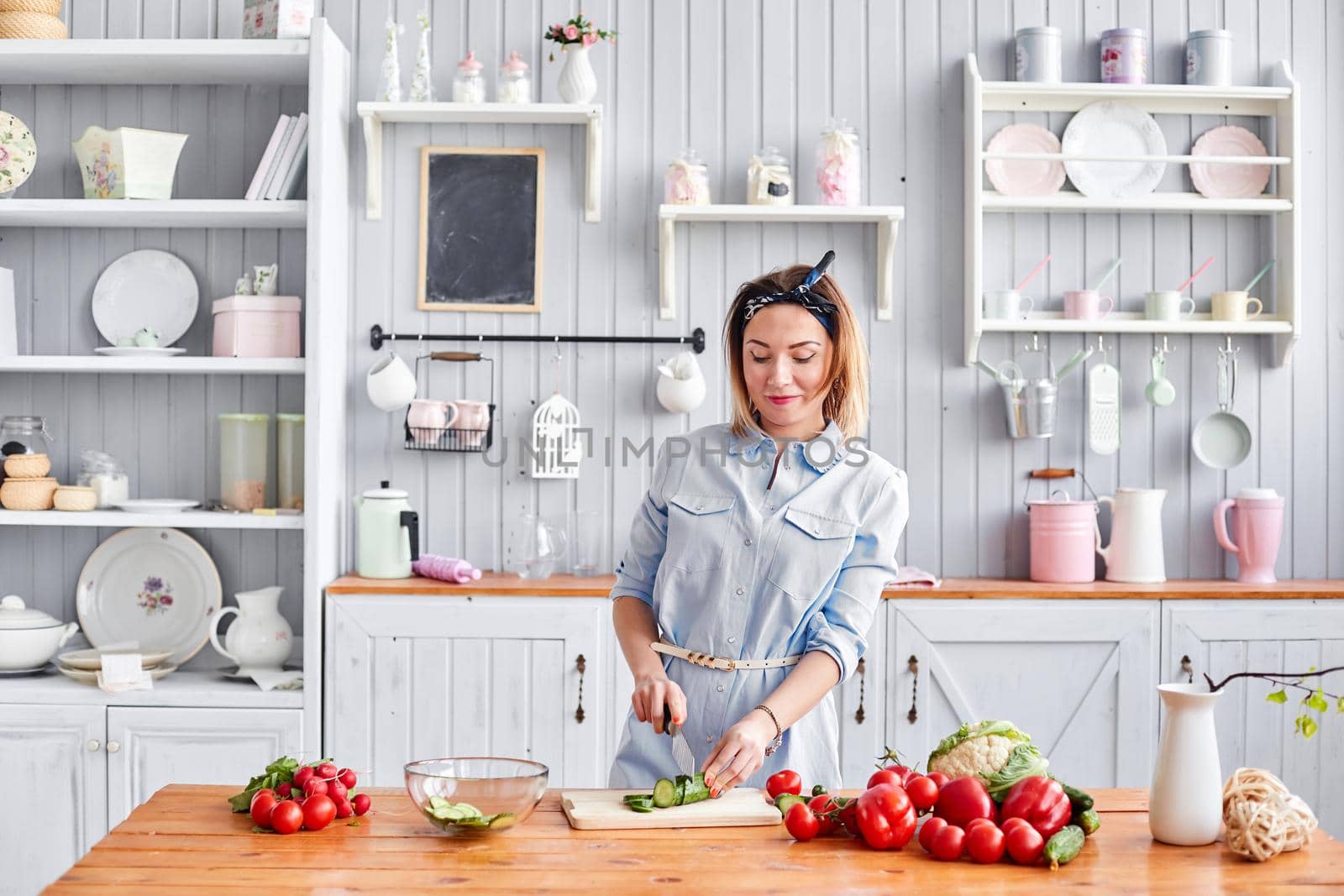 Beautiful young woman is preparing vegetable salad in the kitchen. Healthy Food. Cooking at home. Dieting Concept. by Malkovkosta