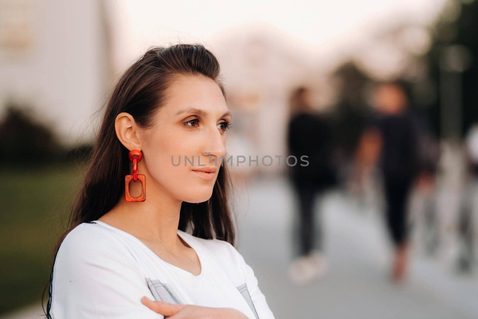 Close-up portrait of a girl with red earrings in white clothes in the city.