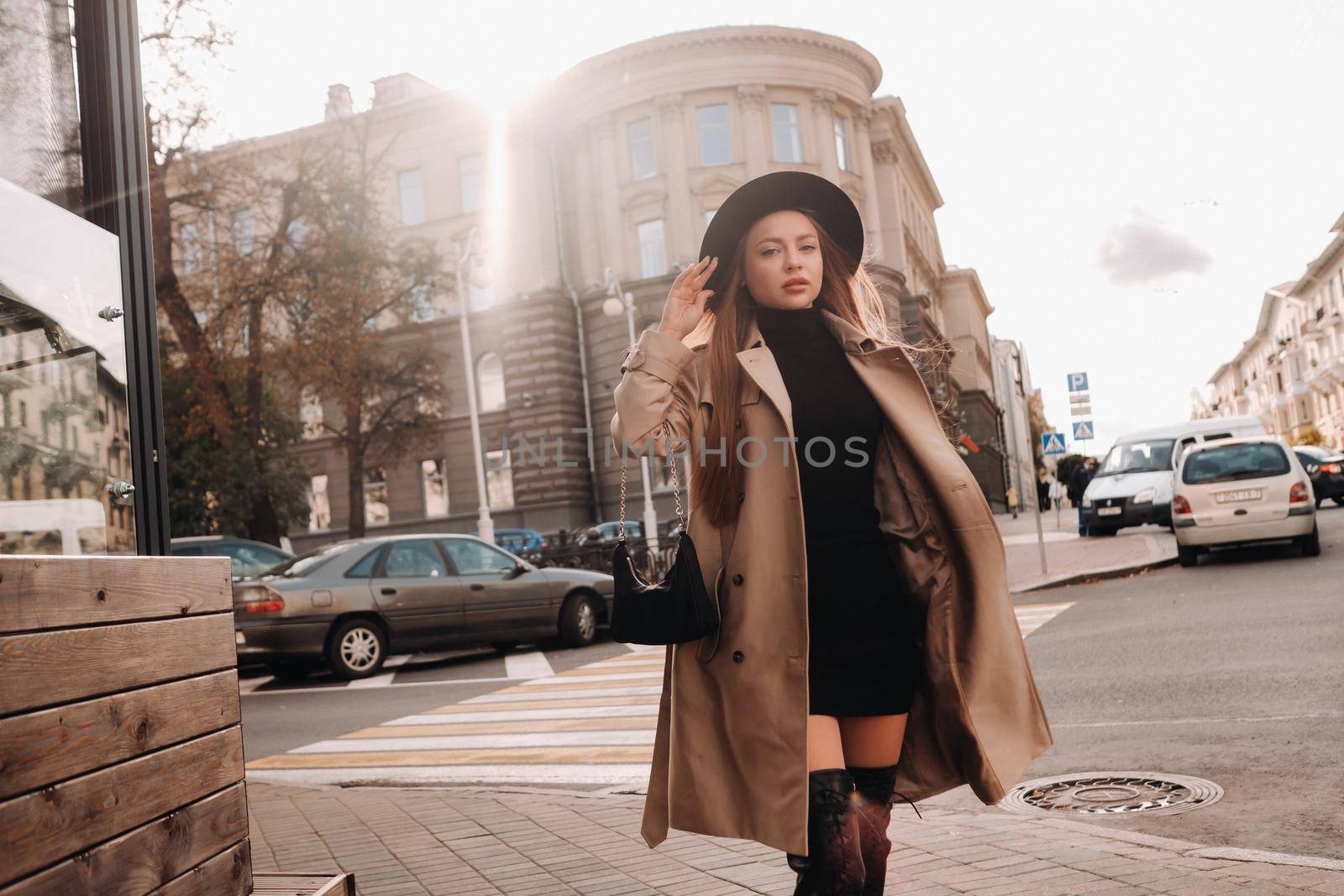 Stylish young woman in a beige coat in a black hat on a city street. Women's street fashion. Autumn clothing.Urban style.