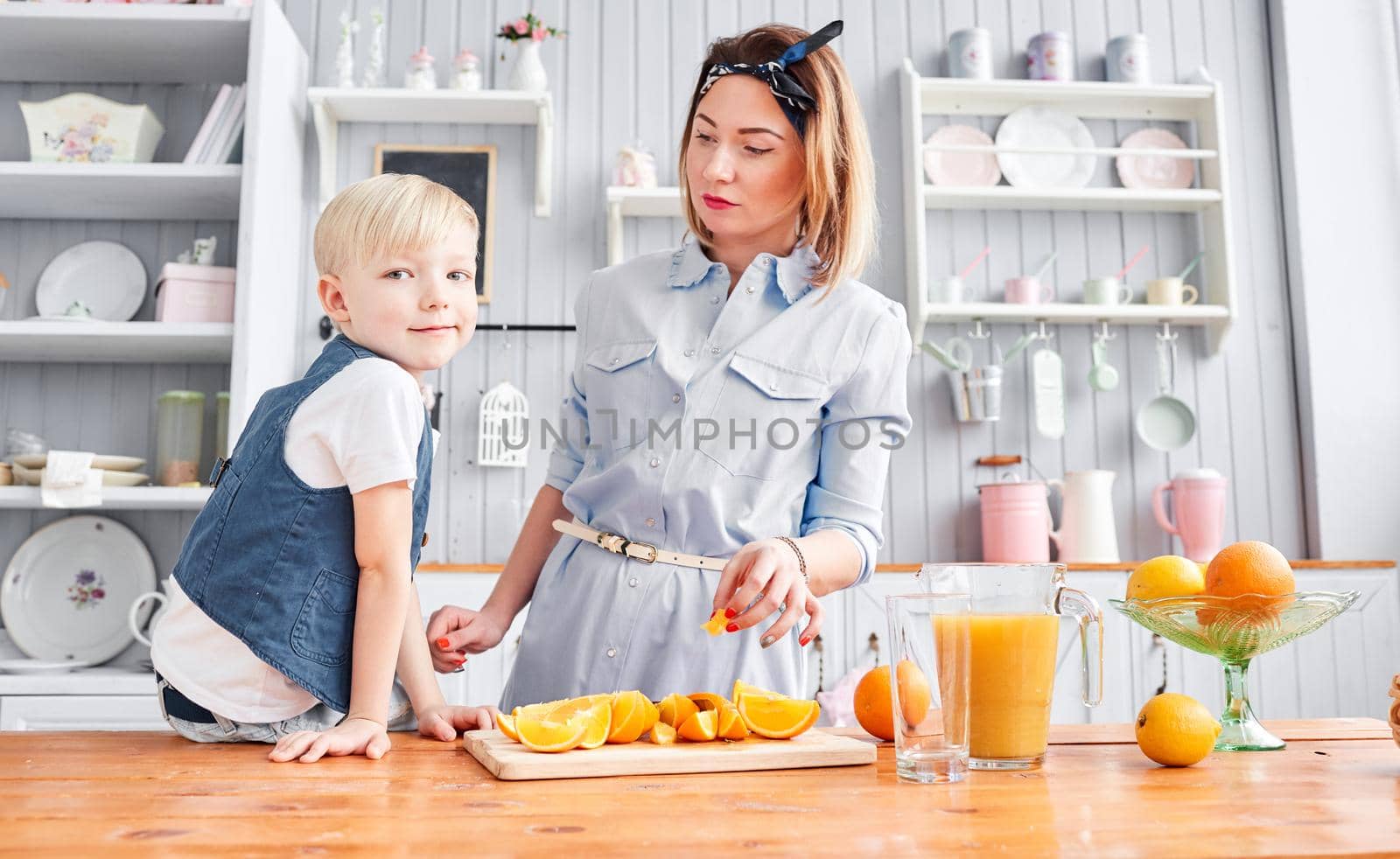 Healthy food, fresh fruit, juicy oranges. Mother and son are smiling while having a breakfast in kitchen. Bright morning in the kitchen. by Malkovkosta