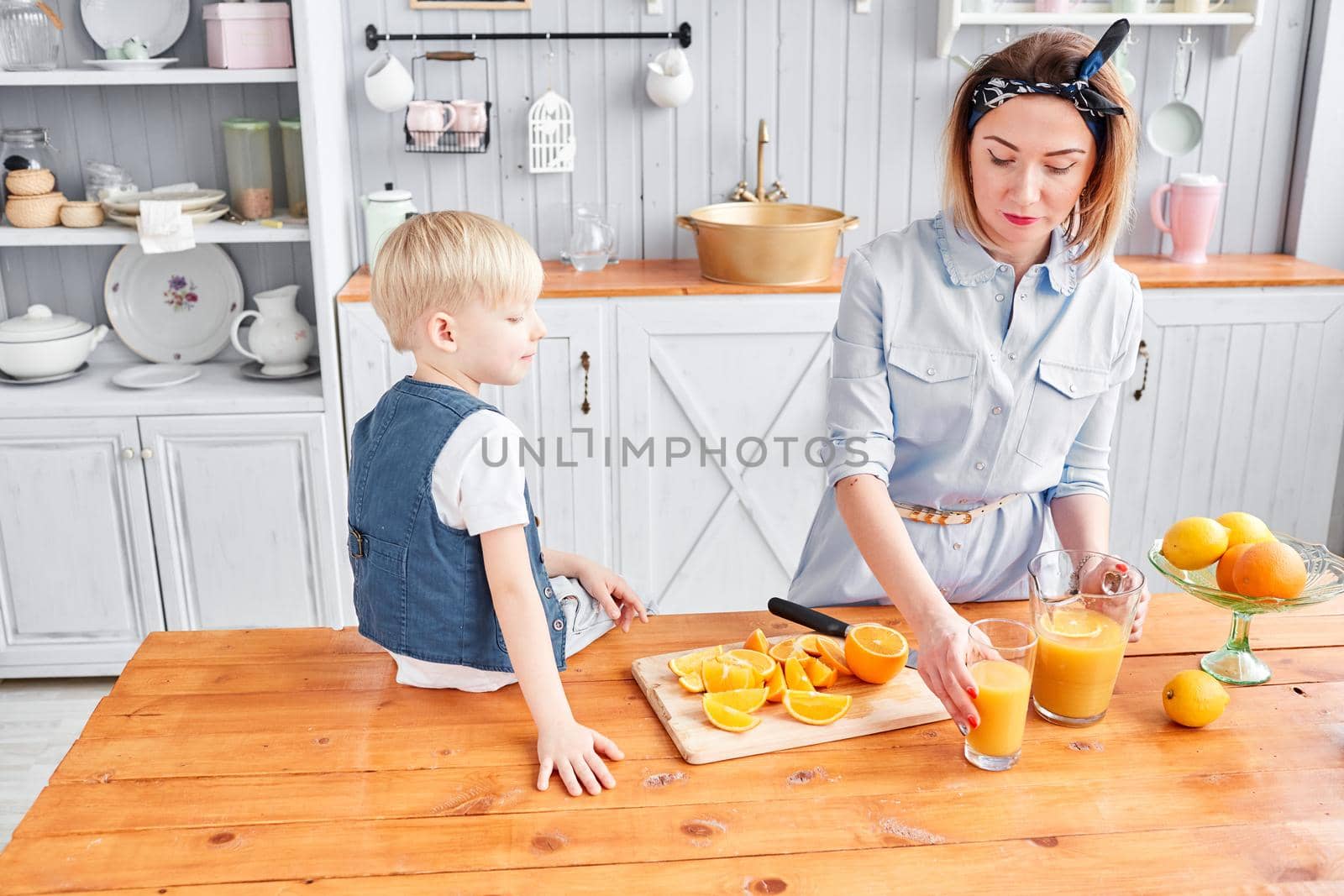 Healthy food, fresh fruit, juicy oranges. Mother and son are smiling while having a breakfast in kitchen. Bright morning in the kitchen. by Malkovkosta