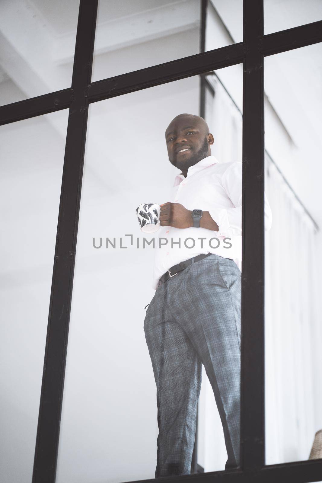 Successful Young Businessman. African American Man Before Trading On Stock Exchange Stay In His Downtown Office With Cup Of Tea. Concept Of Victory, Personal Growth by LipikStockMedia