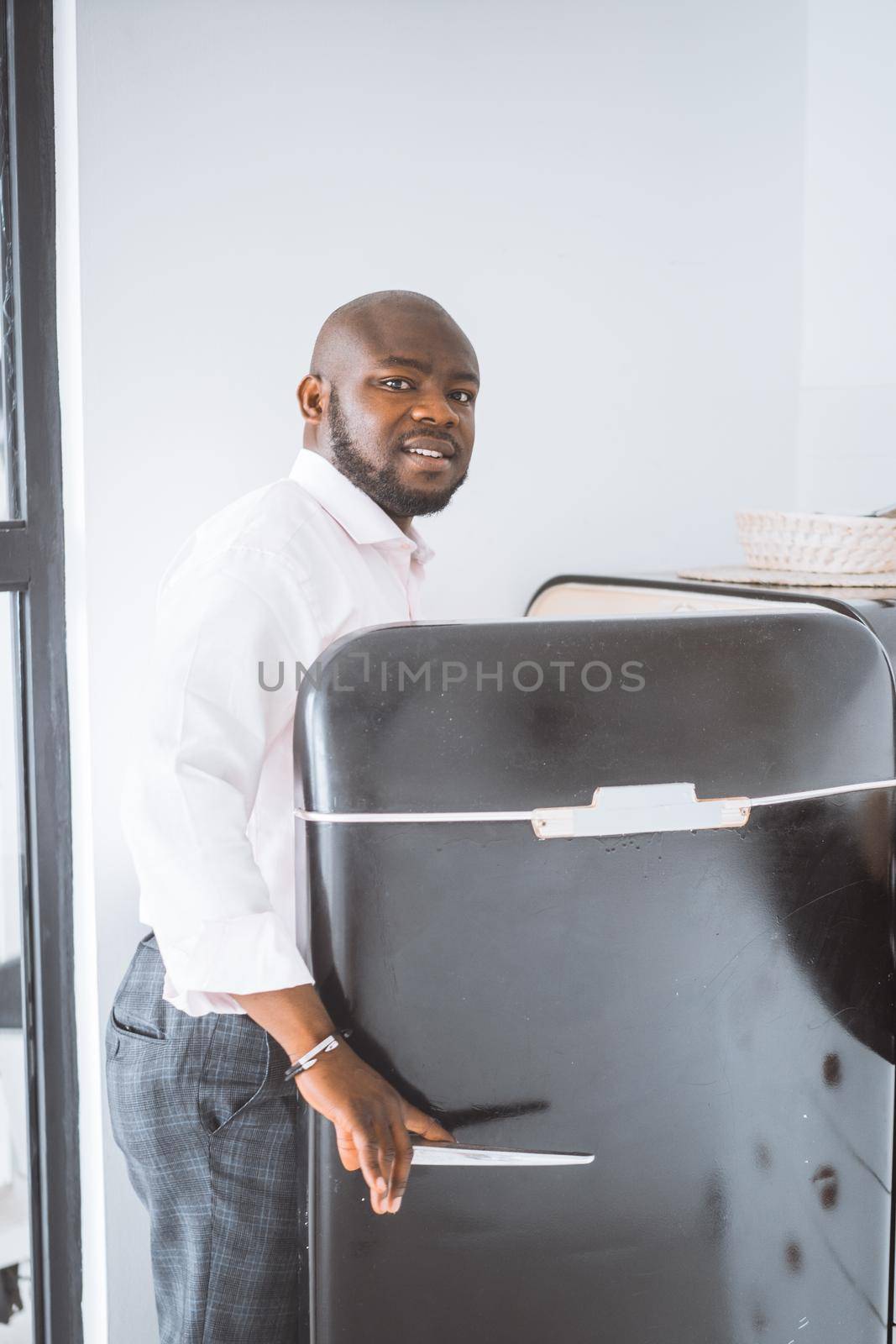 Successful Young Businessman. African American Man Opens Vintage Refrigerator In His Apartment. Concept Of Rich Life, Personal Growth by LipikStockMedia