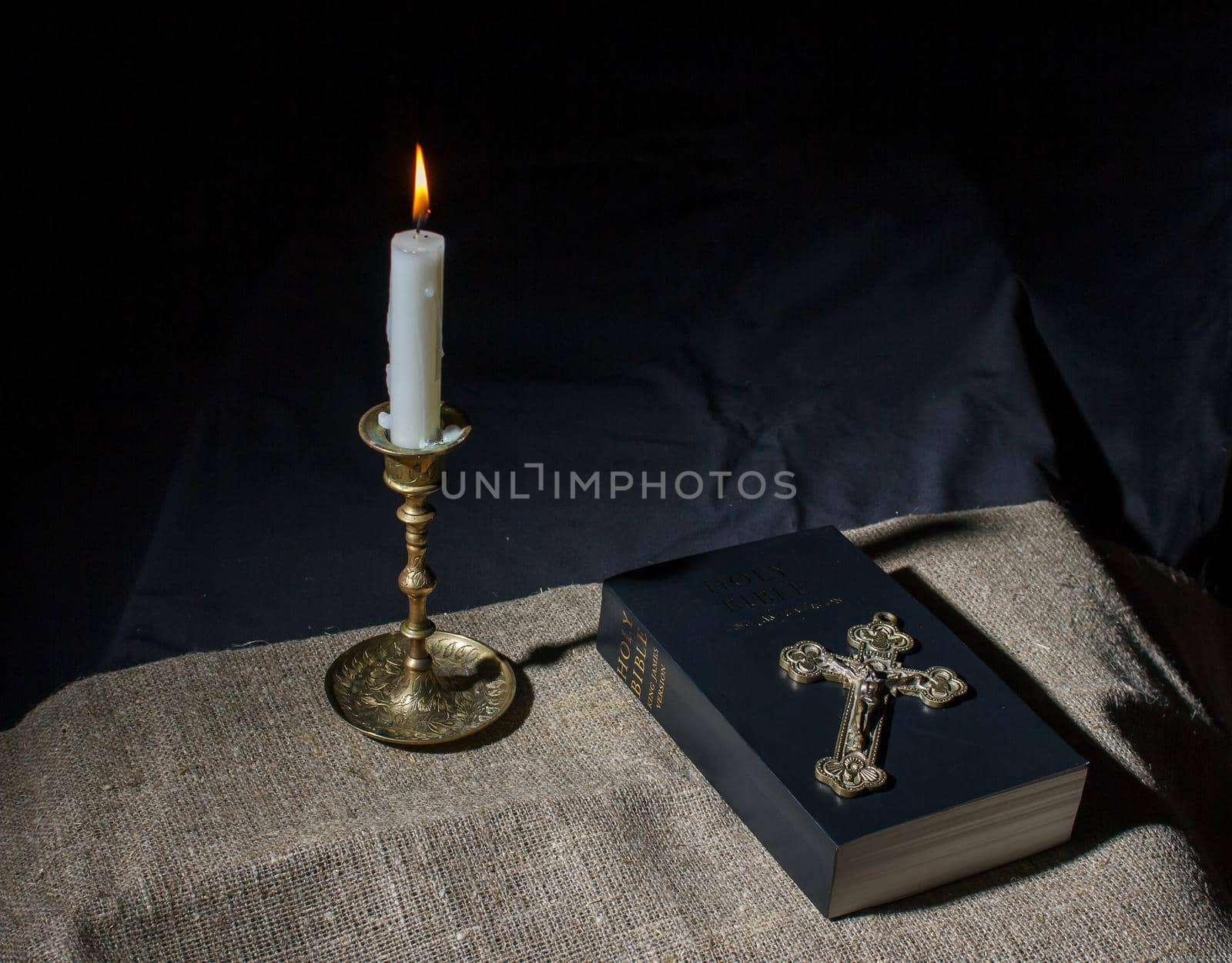 bronze cross, burning candle and bible on the table indoor closeup