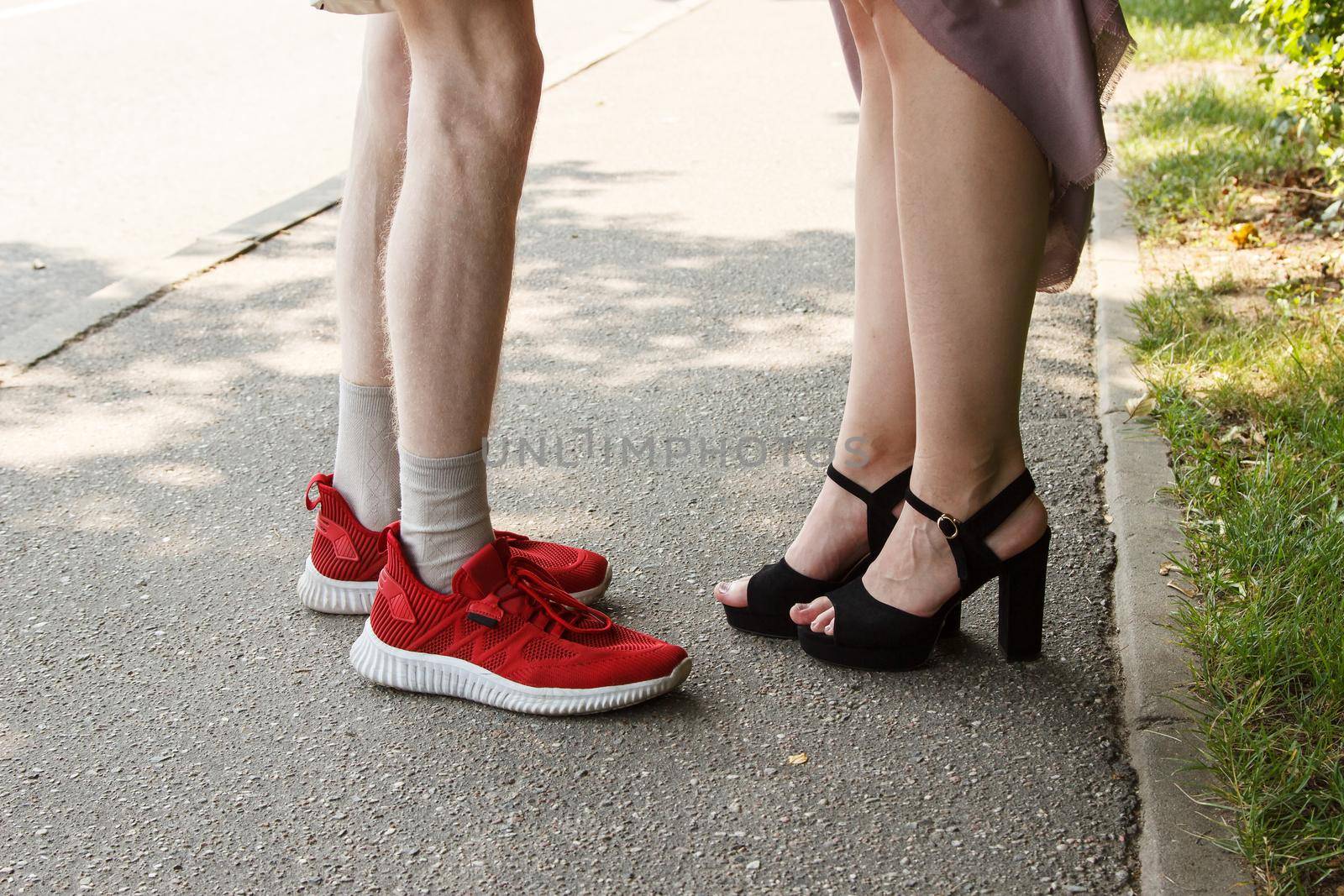 legs of a man and a woman facing each other. standing on sidewalk on summer day