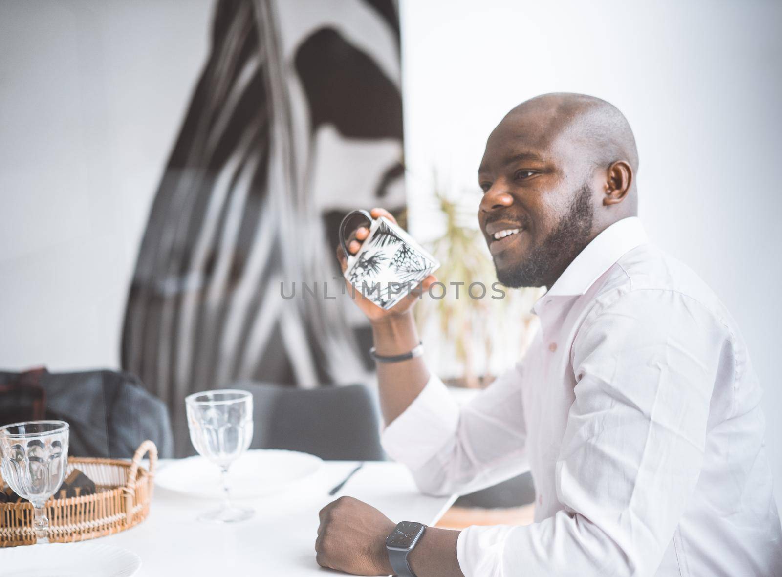 Successful Young Businessman. African American Man Smiling While Sitting At Breakfast In Luxury Apartment. Concept Of Rich Life, Personal Growth by LipikStockMedia