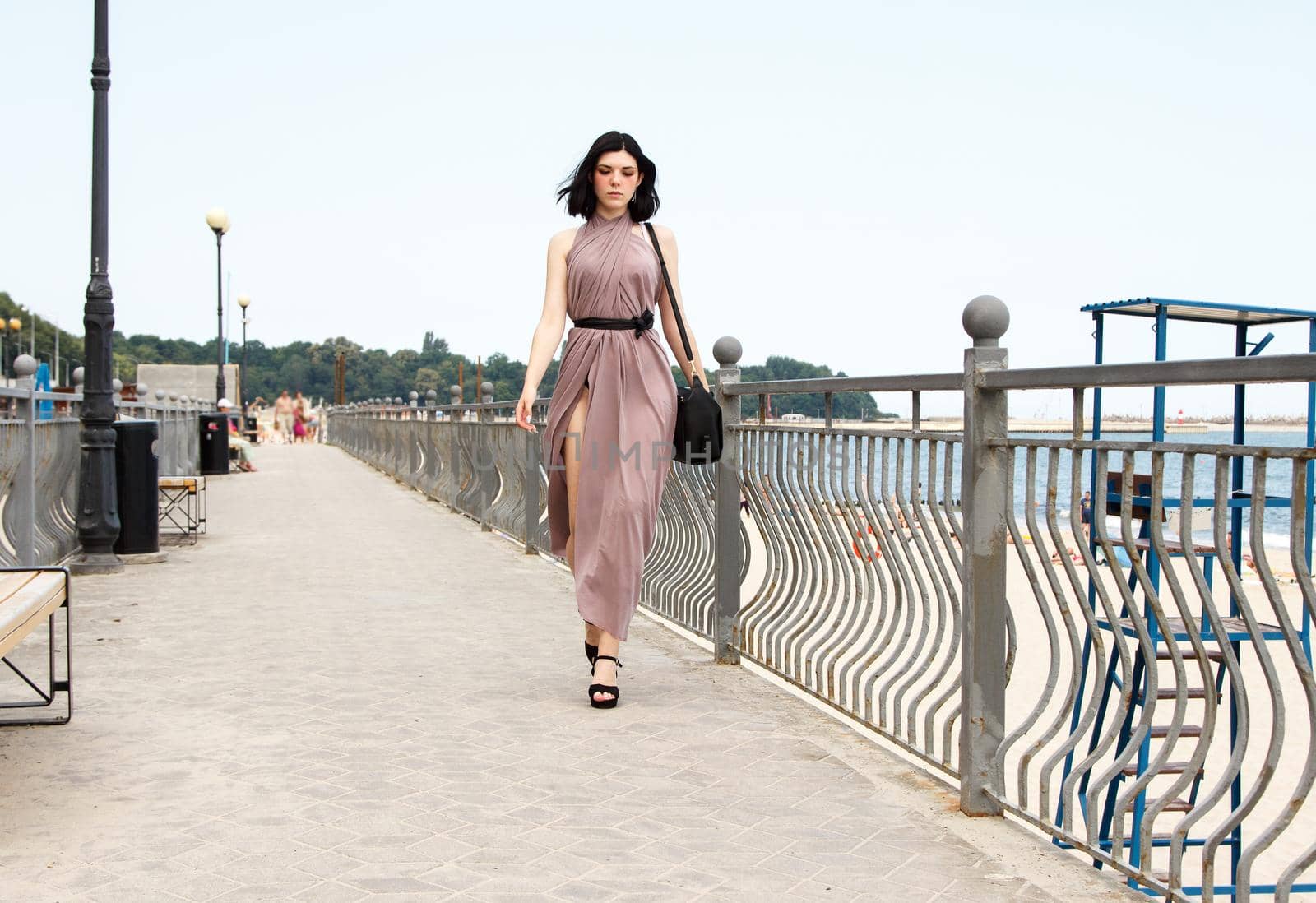 young beautiful brunette woman in beige dress walking on the sidewalk in summer