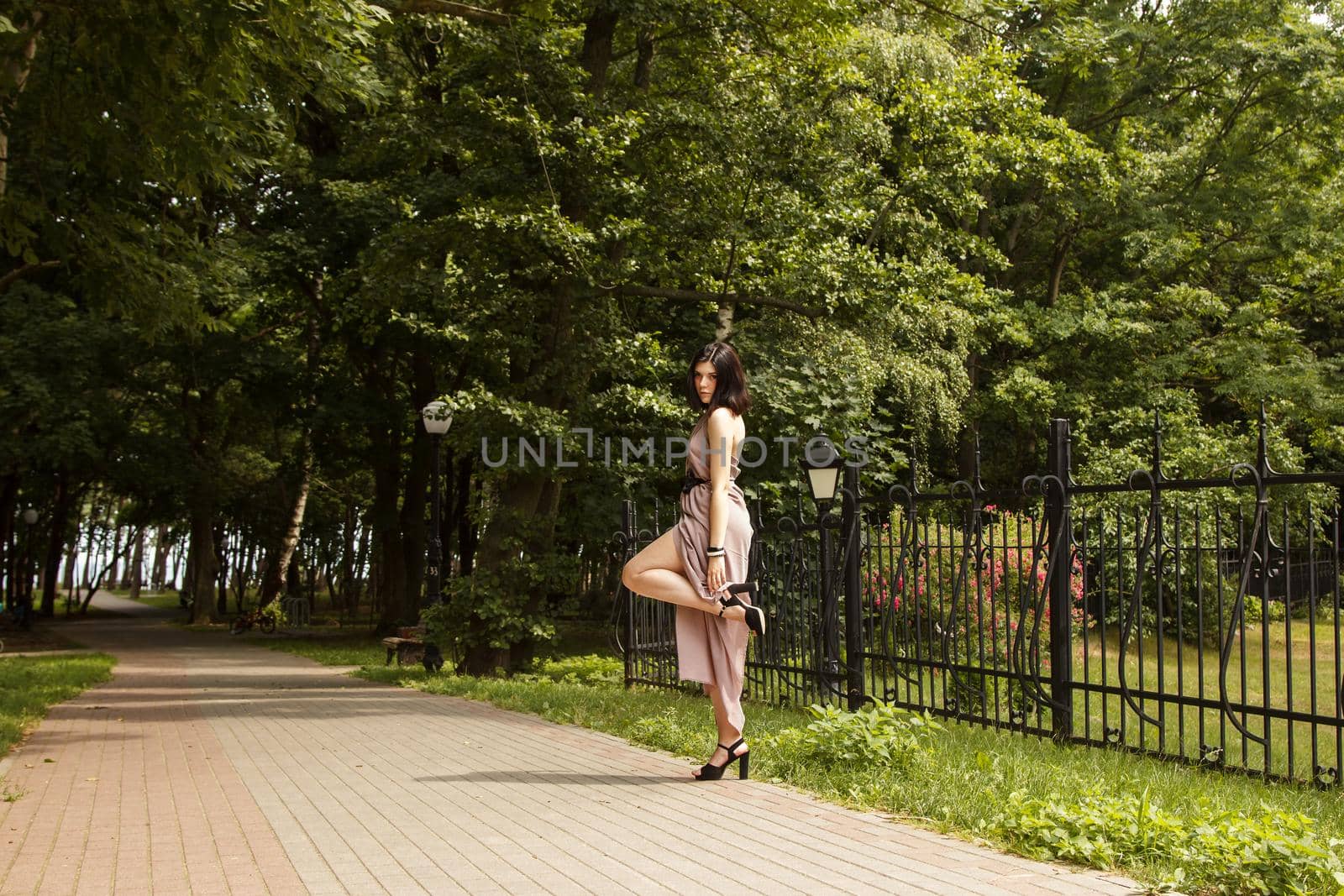 young beautiful brunette woman in beige dress standing on the sidewalk in summer