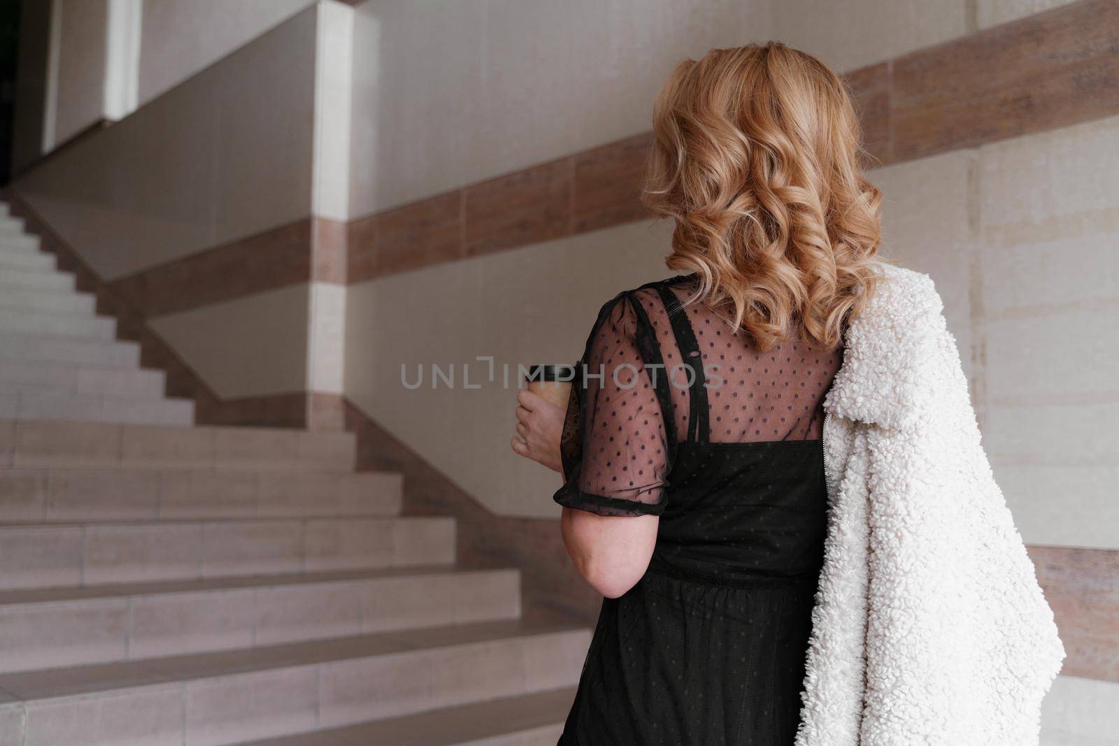 Portrait of a beautiful smiling blonde. She's walking up the stairs, coffee in hand. The Concept Of Urban Life. by Matiunina