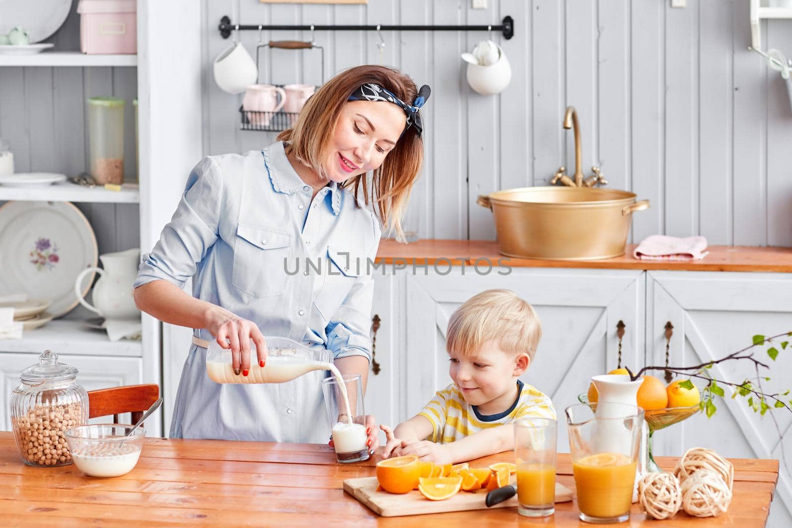 Mother and son are smiling while having a breakfast in kitchen. Mom is pouring milk into glass.