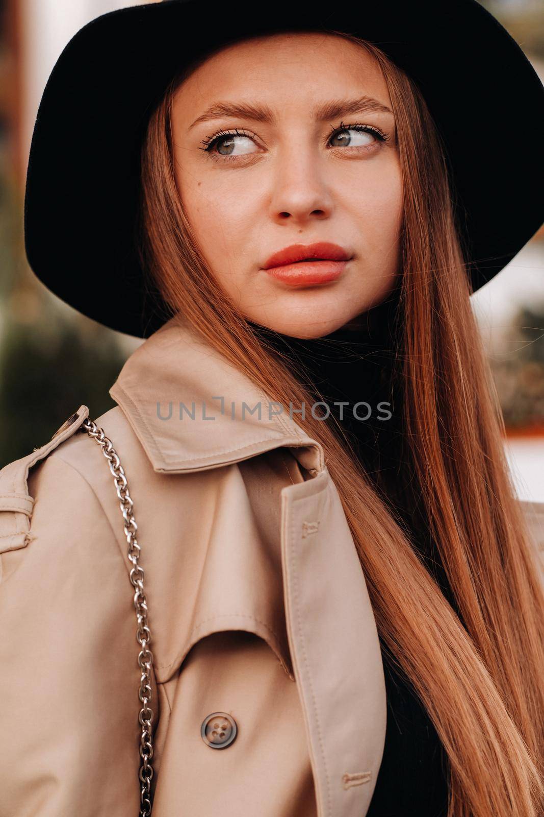 Portrait of a girl in a beige coat and black hat on a city street. Women's street fashion. Autumn clothing.Urban style.