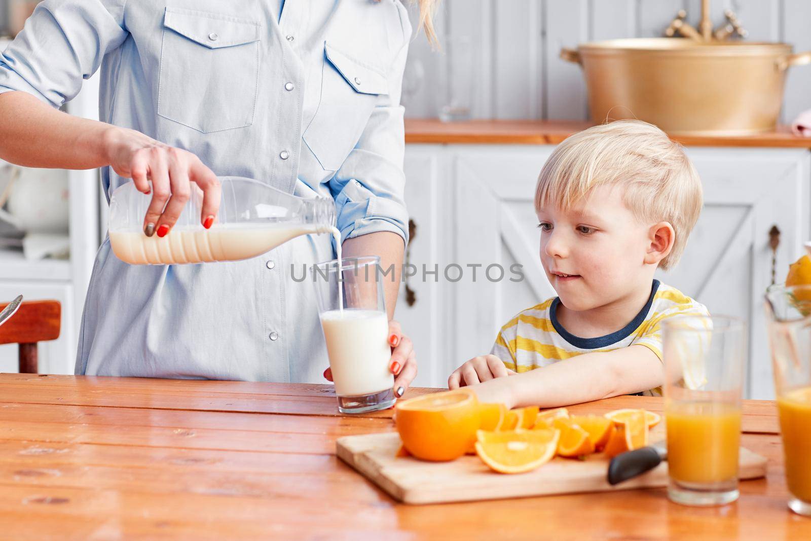 Mother and son are smiling while having a breakfast in kitchen. Mom is pouring milk into glass