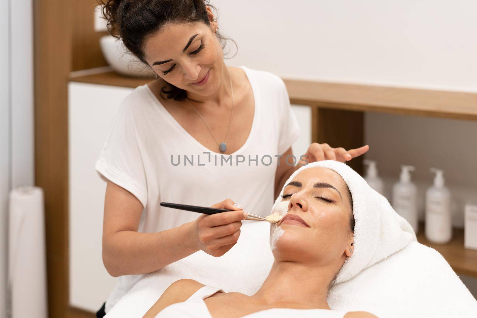 Aesthetics applying a mask to the face of a Middle-aged woman in modern wellness center. Beauty and Aesthetic concepts.