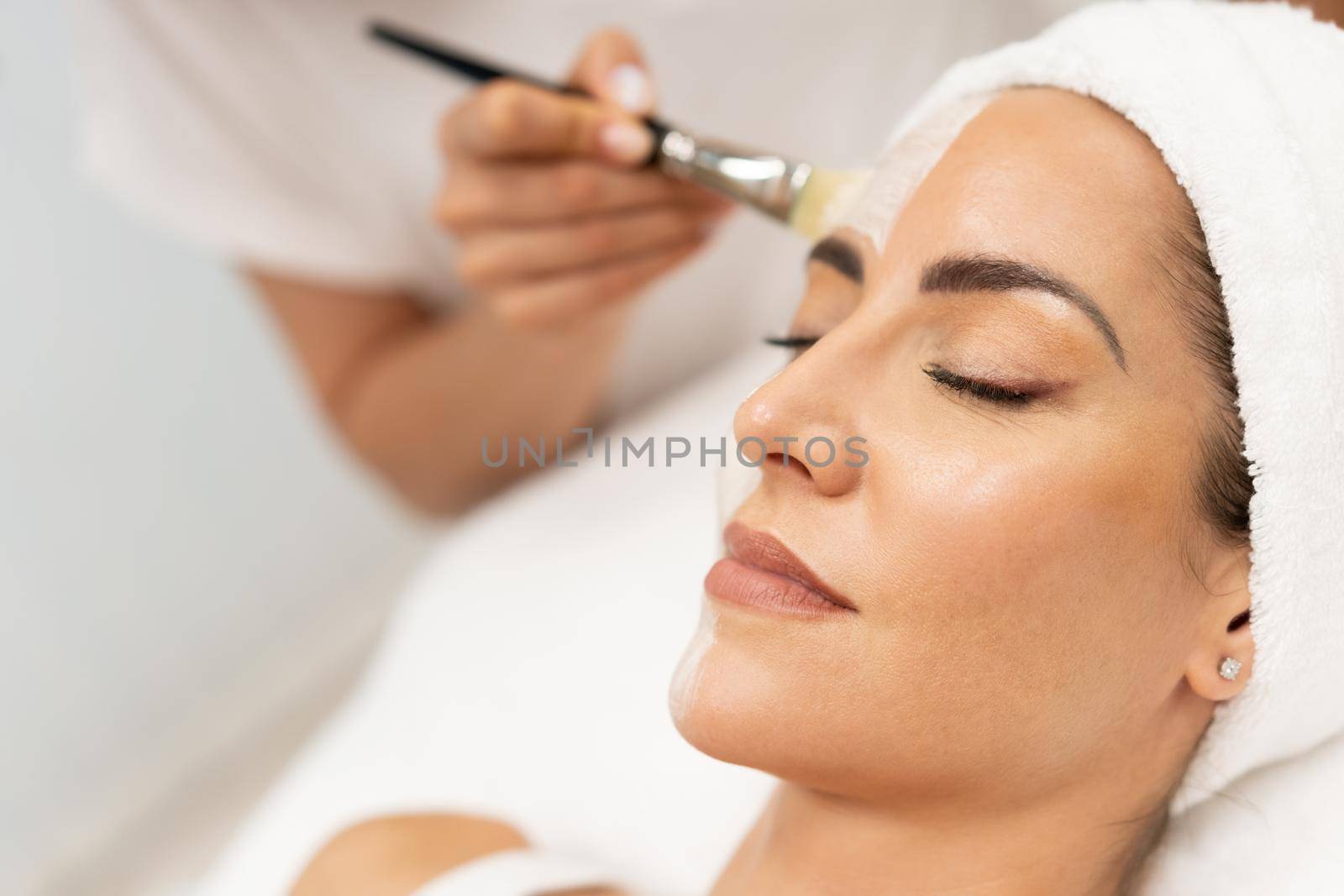 Aesthetics applying a mask to the face of a Middle-aged woman in modern wellness center. Beauty and Aesthetic concepts.