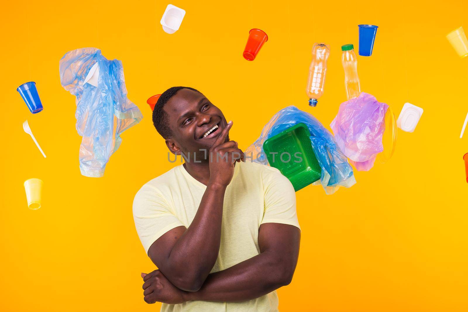 World Environment Day, plastic recycling problem and environmental disaster concept - Surprised african american man looking on trash on yellow.