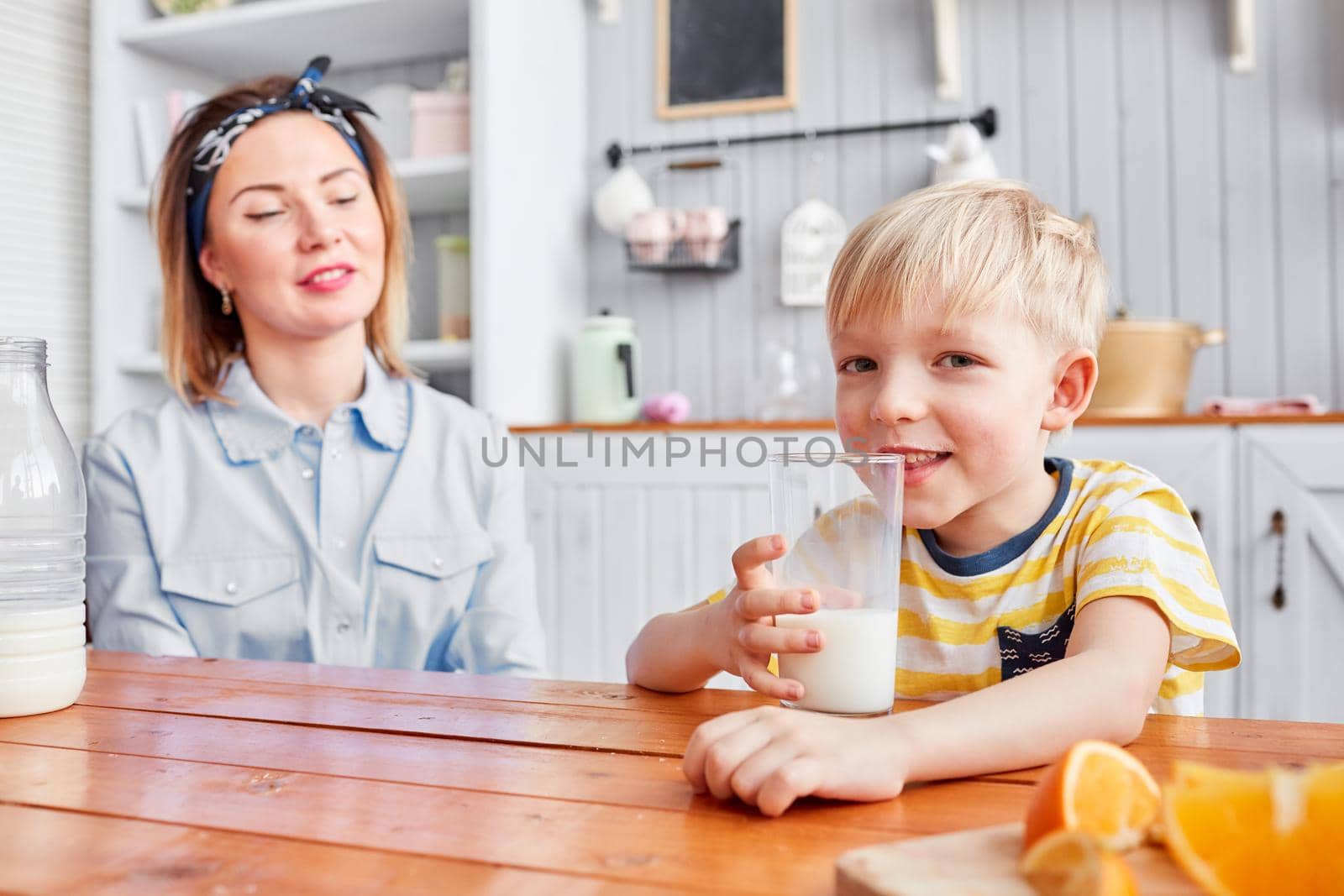 Mother and son are smiling while having a breakfast in kitchen. Bright morning in the kitchen. Healthy Breakfast cereals and fresh fruit. by Malkovkosta