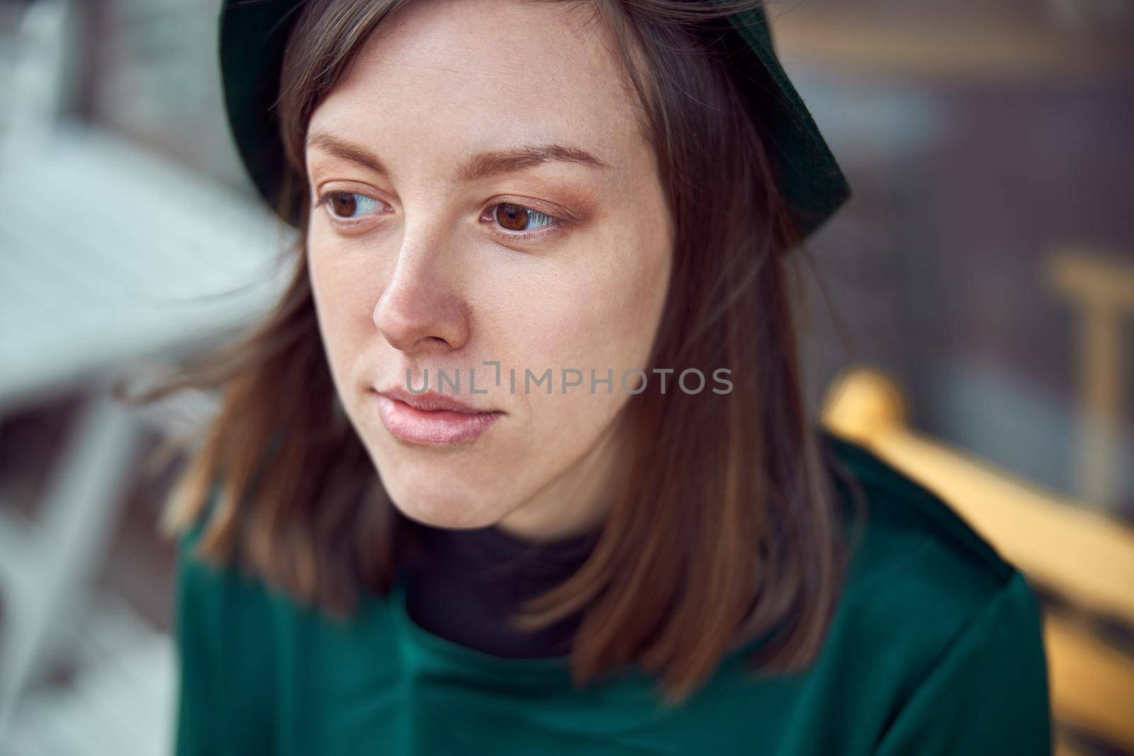 Happy woman in green dress in urban city is sitting near cafe