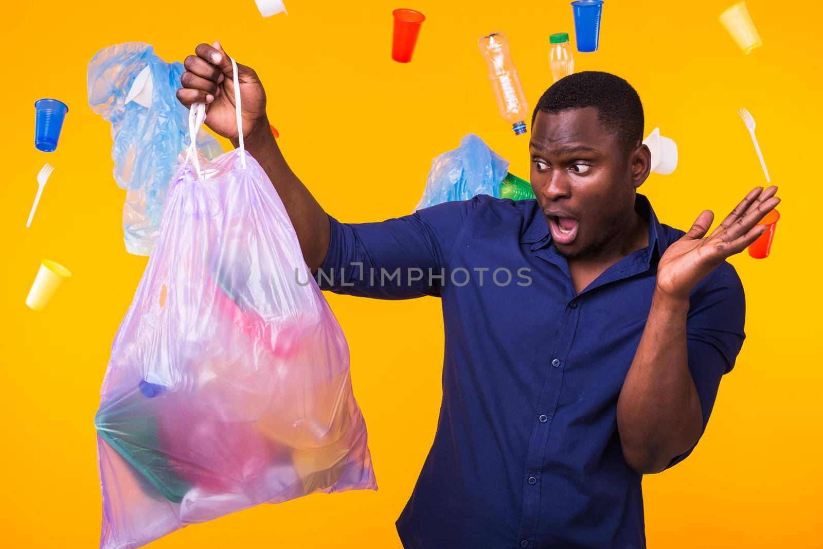 Problem of trash, plastic recycling, pollution and environmental concept - surprised man carrying garbage bag on yellow background.
