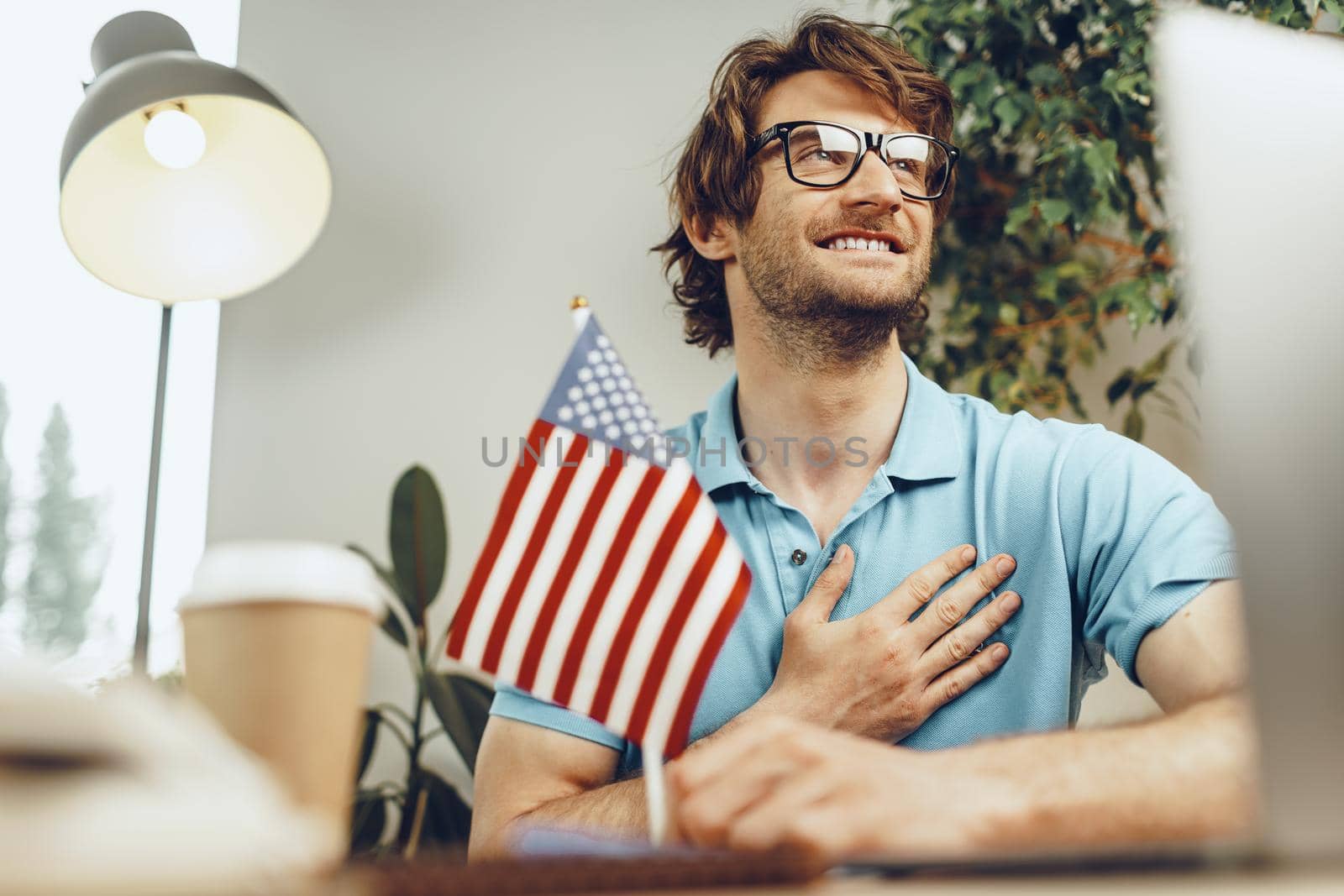 Young bearded businessman sitting at table with laptop and american flag, patriot man