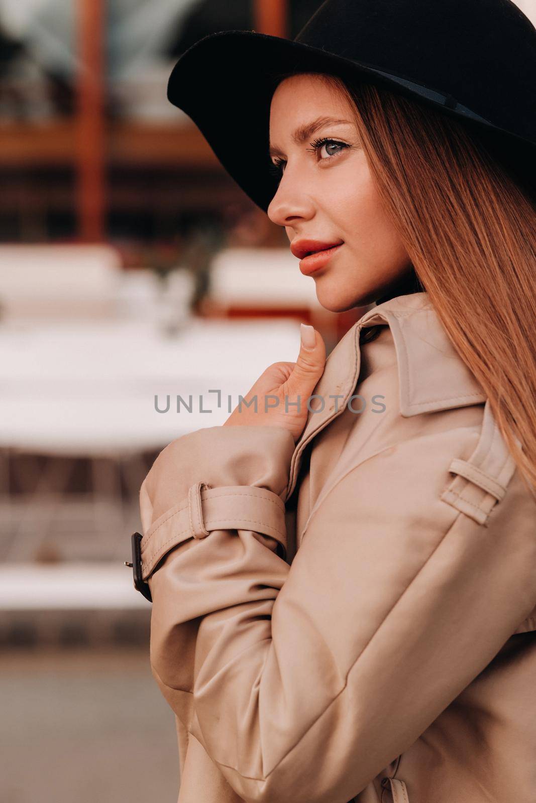 Portrait of a girl in a beige coat and black hat on a city street. Women's street fashion. Autumn clothing.Urban style by Lobachad