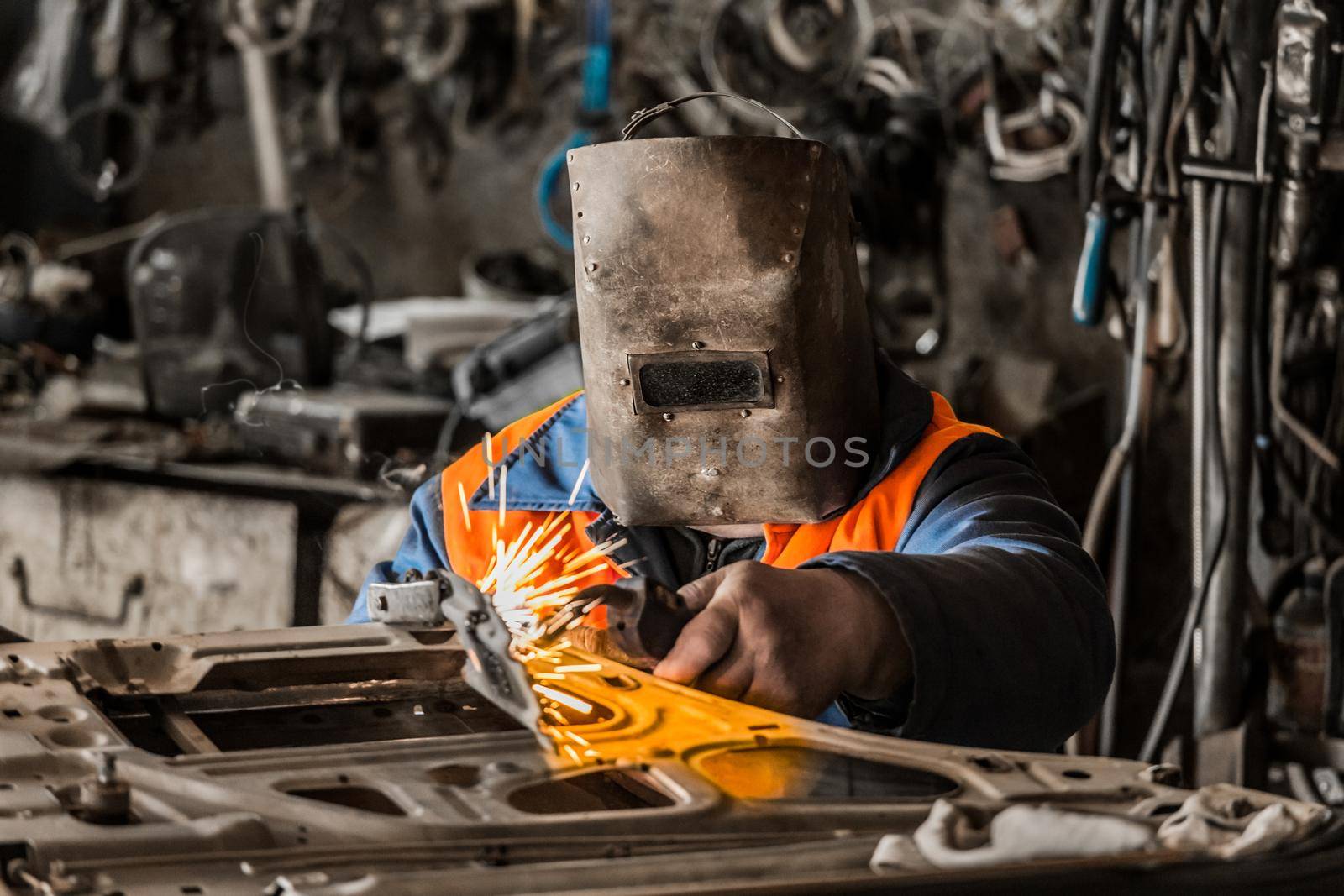 Welder man in the shield is engaged in welding work and metal work repairs the car door in the workshop by AYDO8