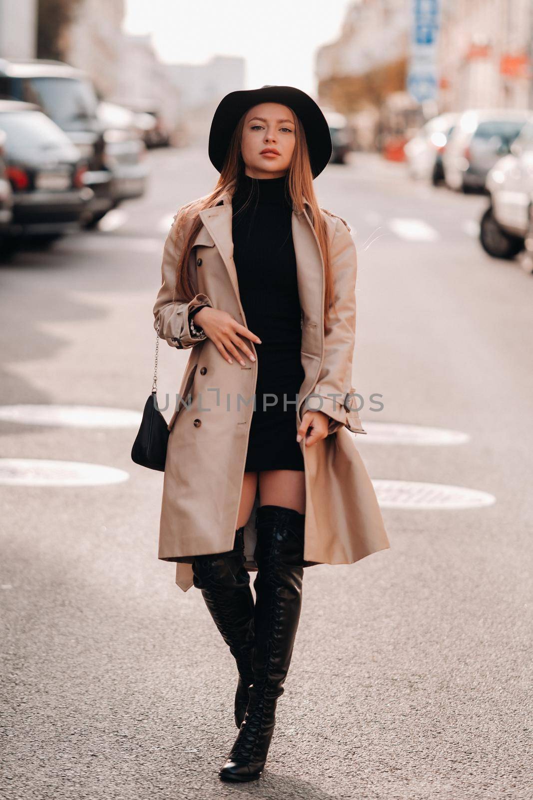 Stylish young woman in a beige coat in a black hat on a city street. Women's street fashion. Autumn clothing.Urban style.