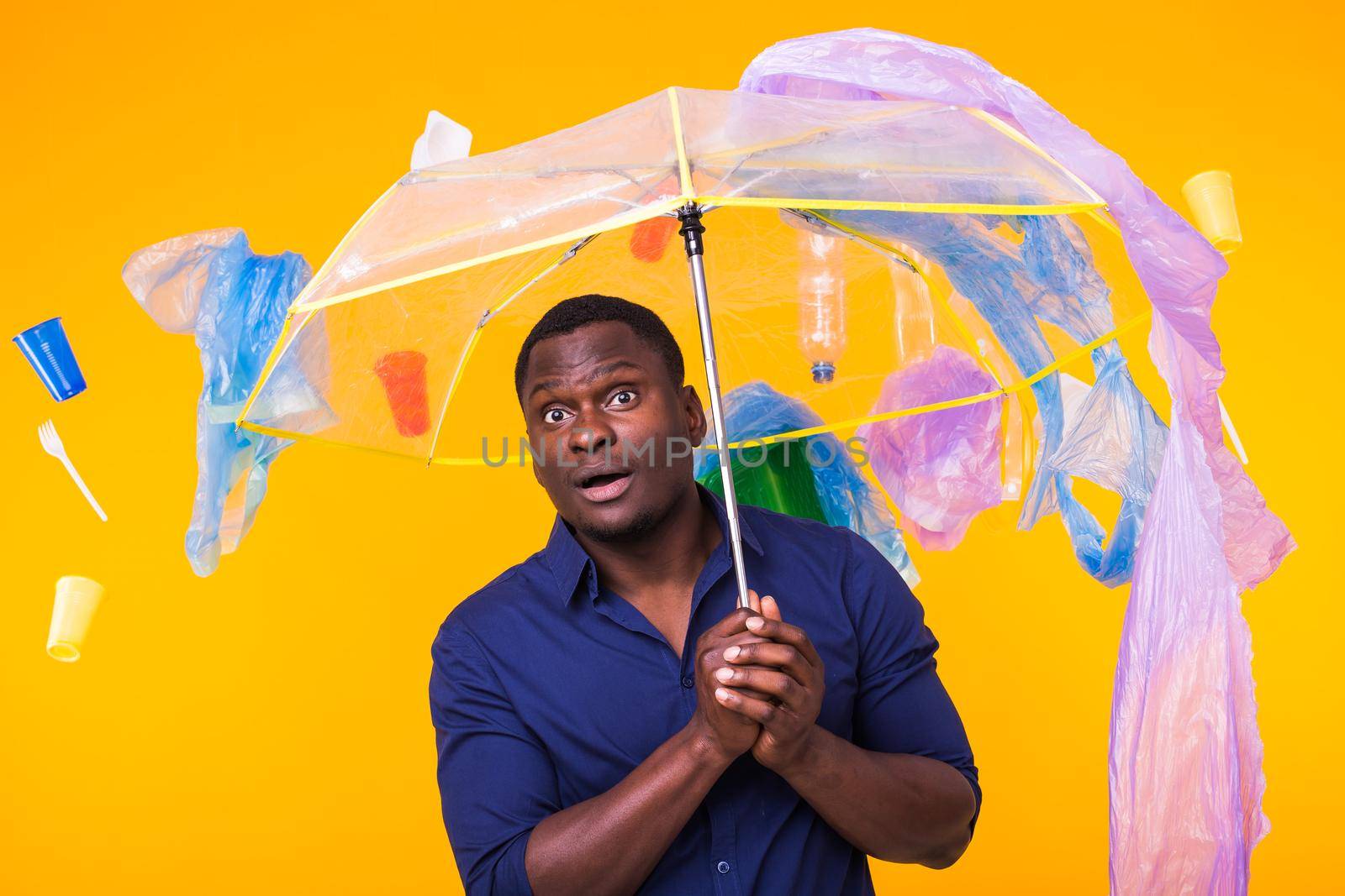 Plastic recycling problem, ecology and environmental disaster concept - Surprised african american man on yellow background with trash. He's worried about ecology disaster