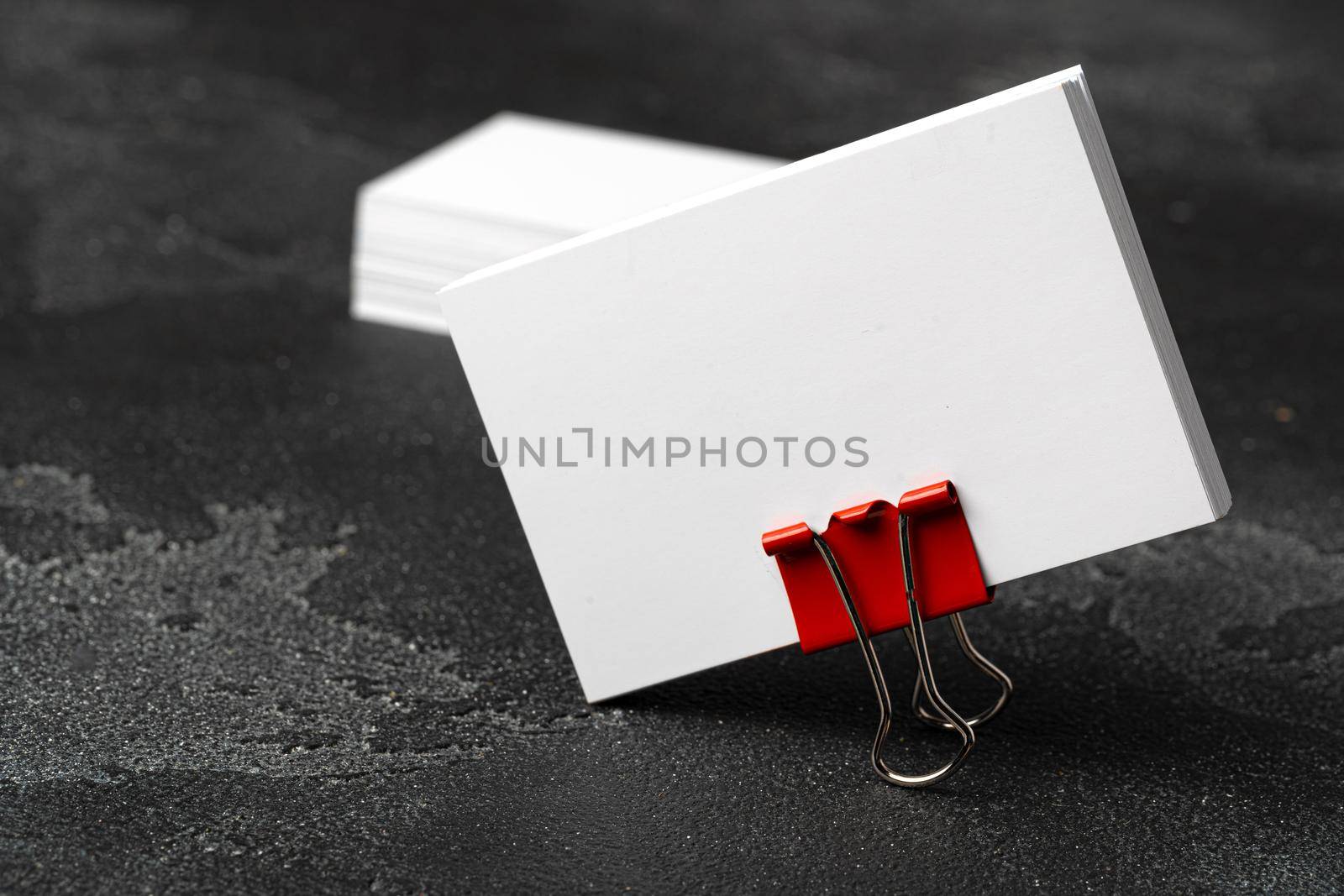 White businesscards united with a paper clip on a black rough background, copy space