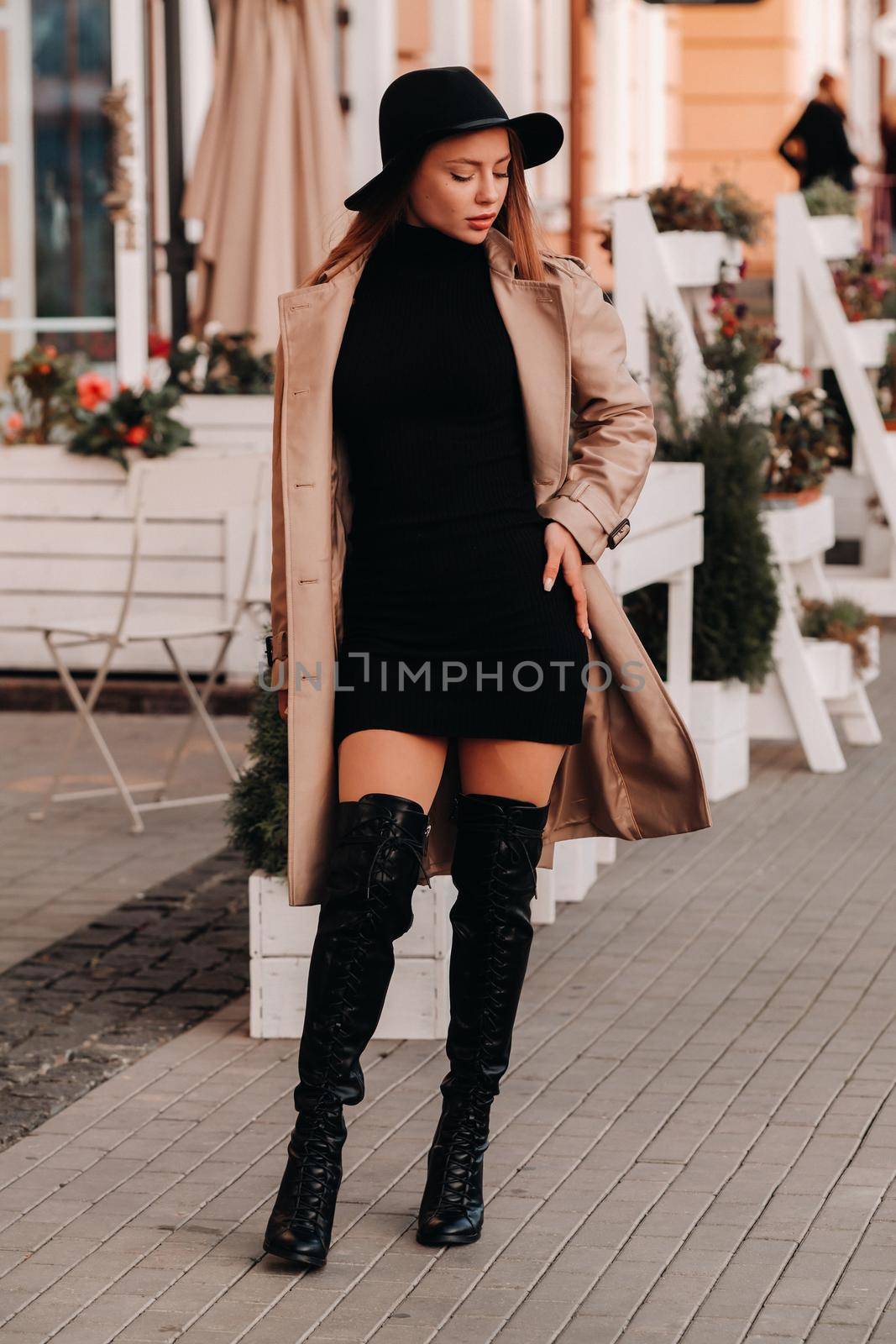 Stylish young woman in a beige coat in a black hat on a city street. Women's street fashion. Autumn clothing.Urban style.