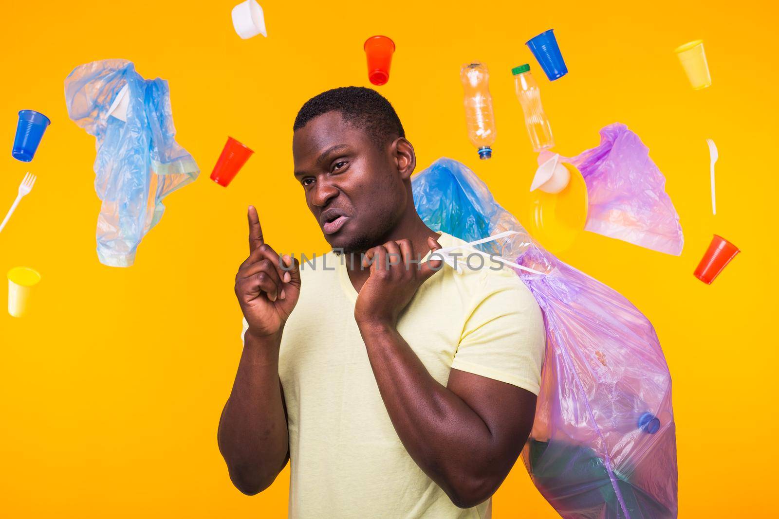 Problem of trash, plastic recycling, pollution and environmental concept - african american man carrying garbage for recycling and pointing up on yellow.