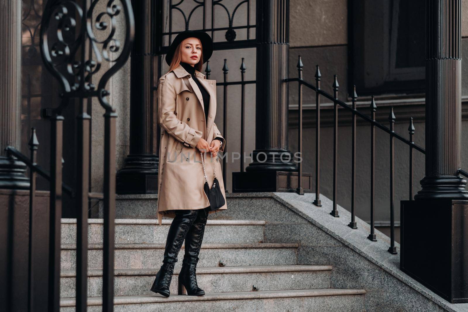 Stylish young woman in a beige coat in a black hat on a city street. Women's street fashion. Autumn clothing.Urban style.