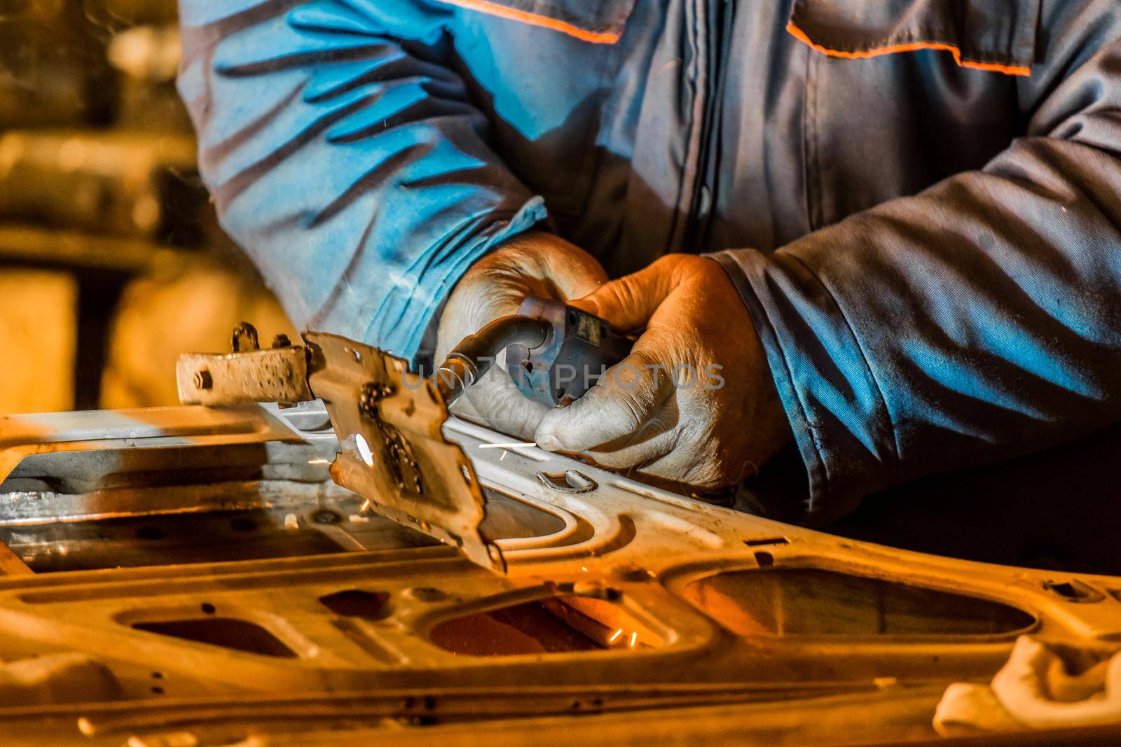 The hands of a male industrial welder worker hold a welding machine, and are engaged in welding on metal and repairing a car door in a workshop at the plant.