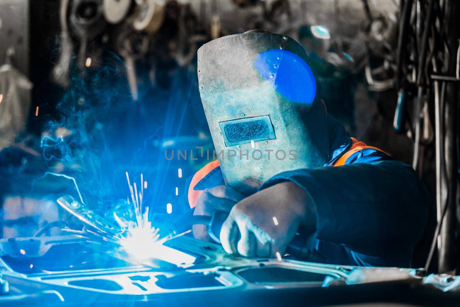 Welder man in a protective mask of iron is engaged in the process of welding and metal work in the workshop of an industrial plant.