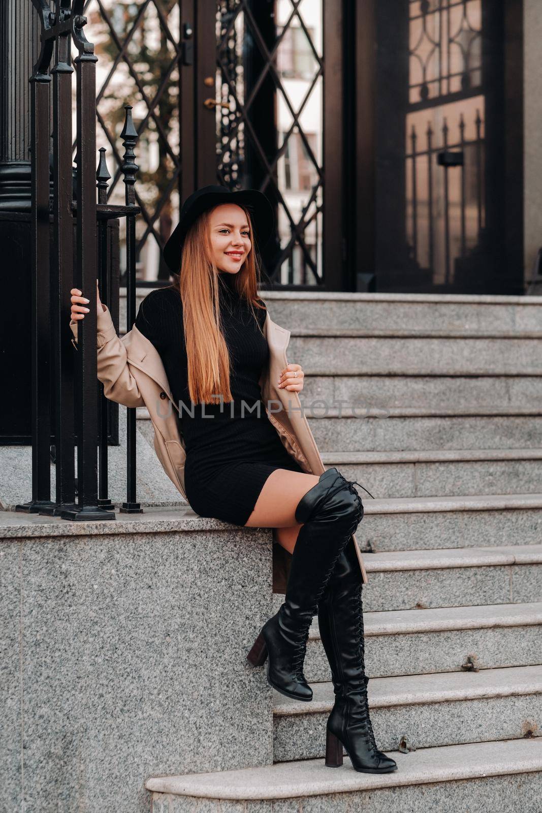 Stylish young woman in a beige coat in a black hat on a city street. Women's street fashion. Autumn clothing.Urban style.