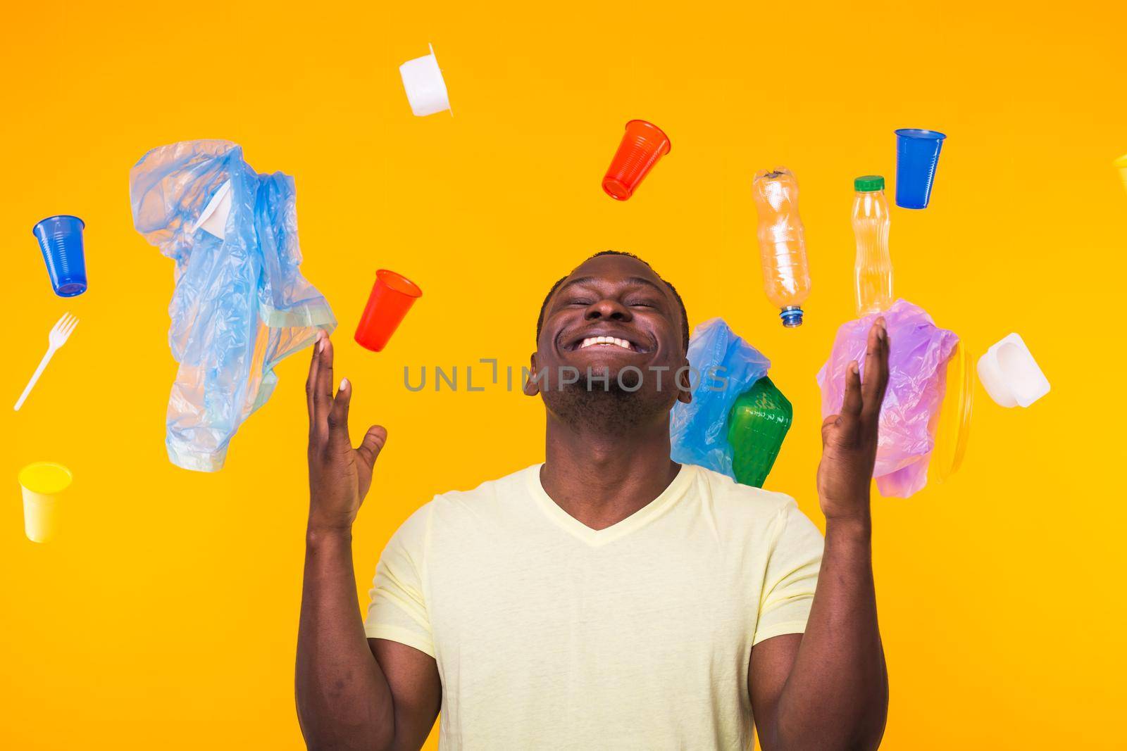 Plastic recycling problem, ecology and environmental disaster concept - Surprised african american man on yellow background with trash. He's worried about ecology disaster