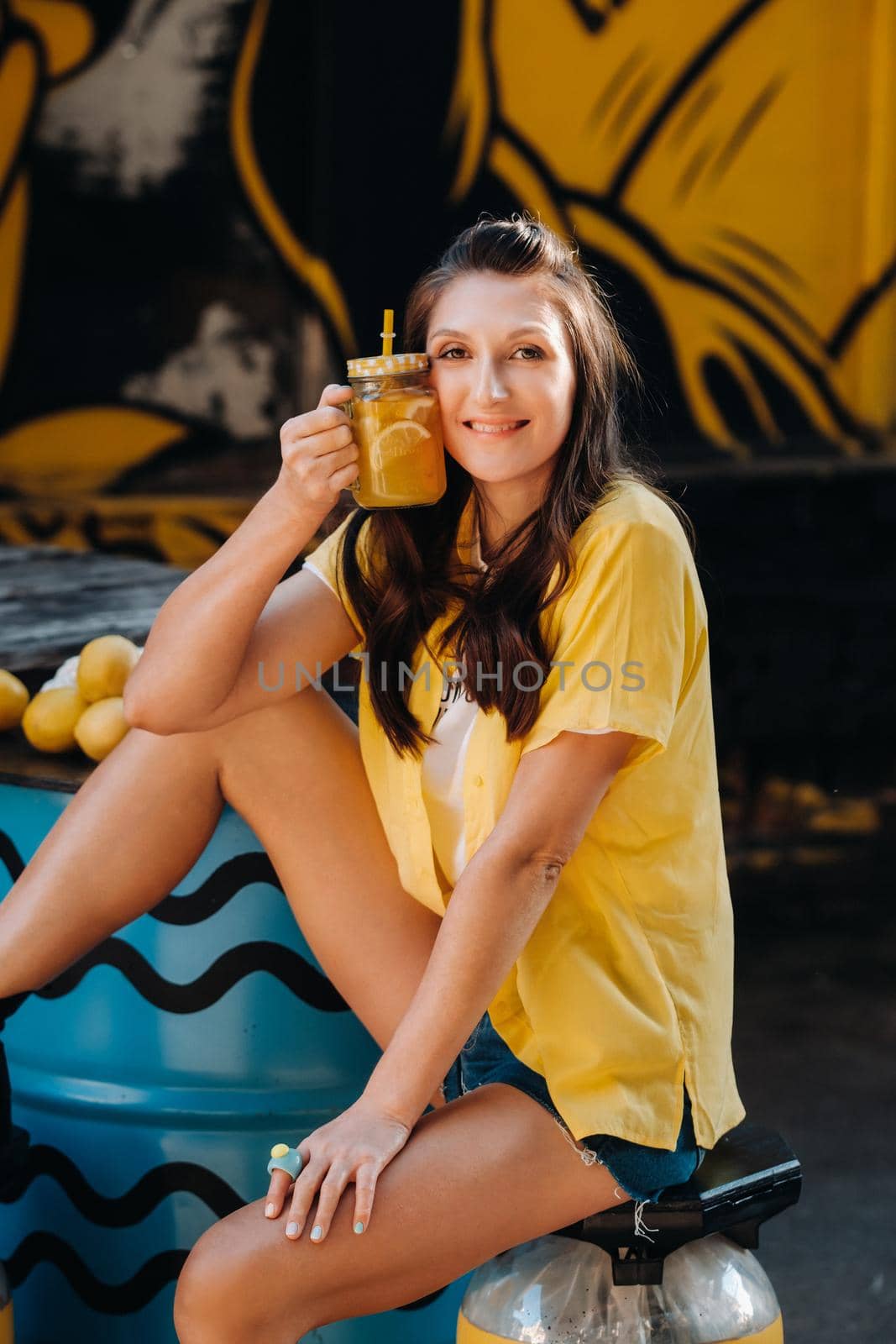 a girl in a yellow shirt with lemon juice in her hands in a city cafe on the street. Portrait of a woman in yellow.