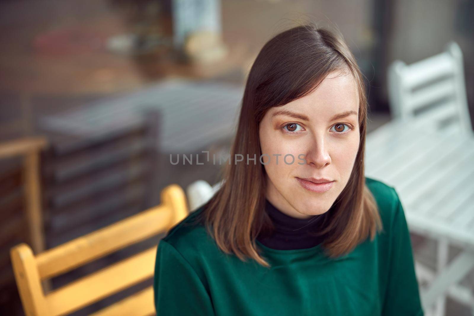 Portrait of cheerful young caucasian woman in green clothes that sitting outside cafe