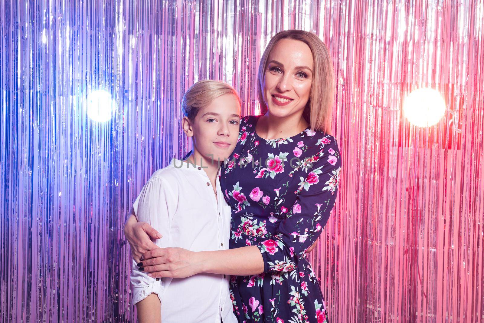 Mothers day, children and family concept - teen boy and his mom embracing on shiny party background