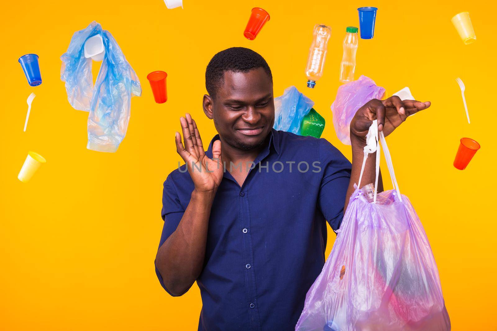 Problem of trash, plastic recycling, pollution and environmental concept - confused man carrying garbage bag on yellow background by Satura86