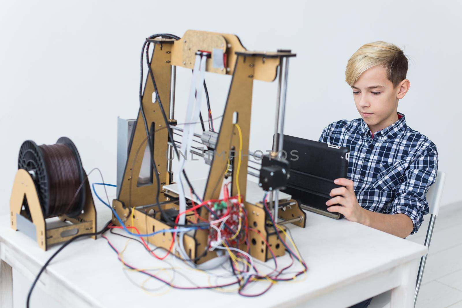 Education, children, technology concept - teen boy is printing on 3d printer