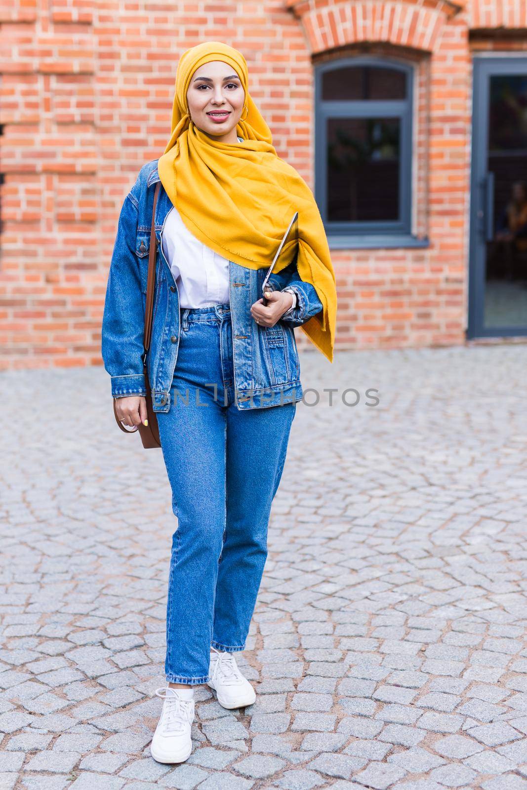 Arab woman student. Beautiful muslim female student wearing yellow hijab holding tablet