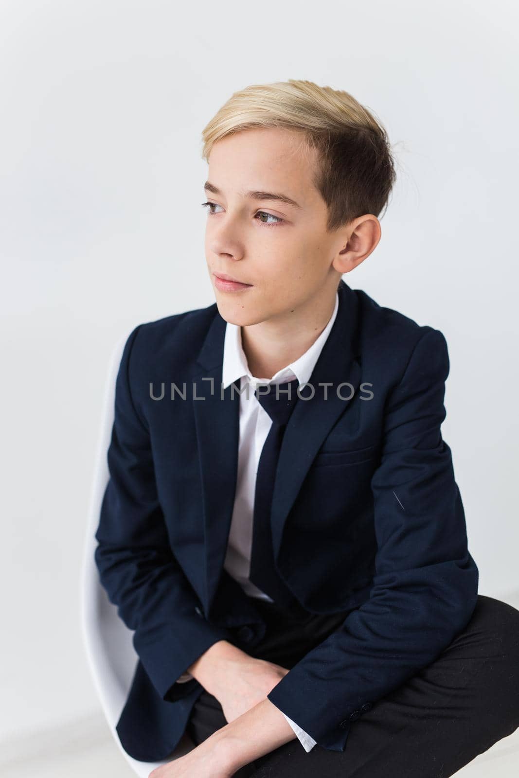 Portrait of stylish school boy teenager in white shirt and jacket against white background with copy space