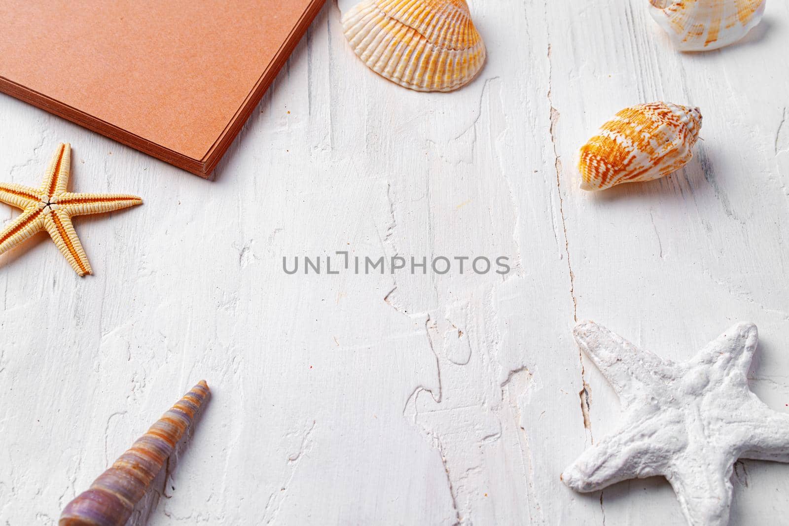 Brown open notepad surrounded by sea shells on white wooden table, copy space